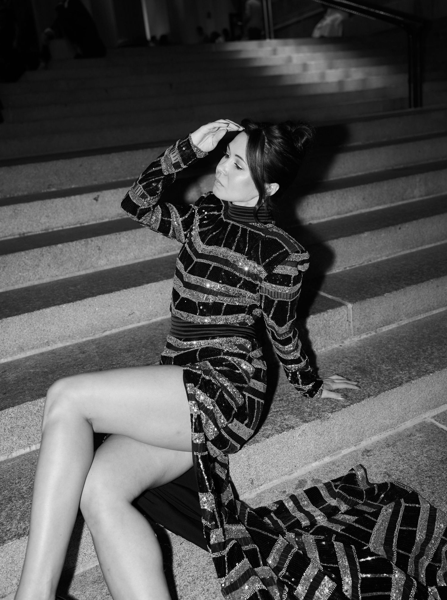 Black and white photo of a woman in a sequined dress posing on steps.