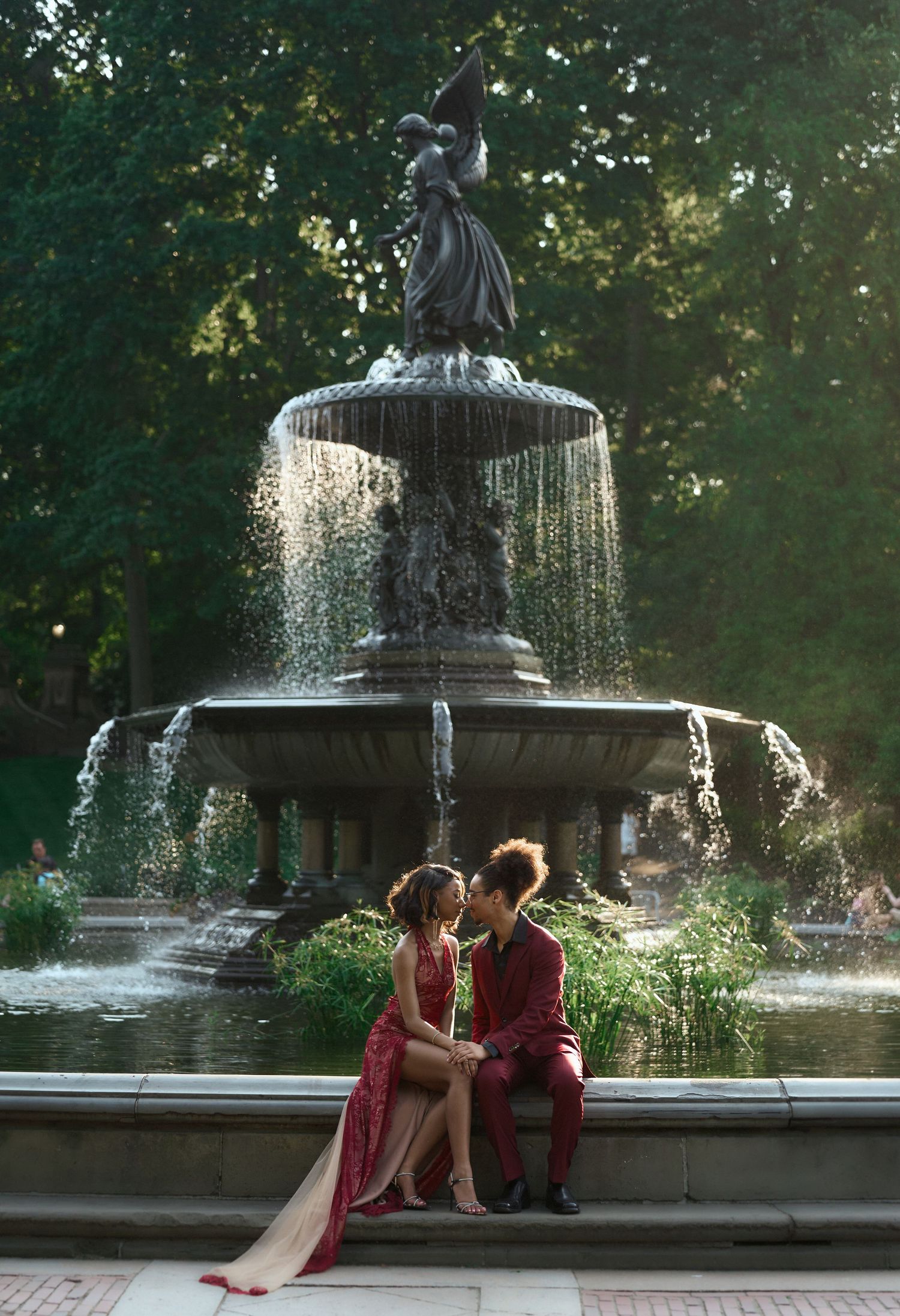 Couple in matching red formal wear share romantic moment at Bethesda Fountain in Central Park.