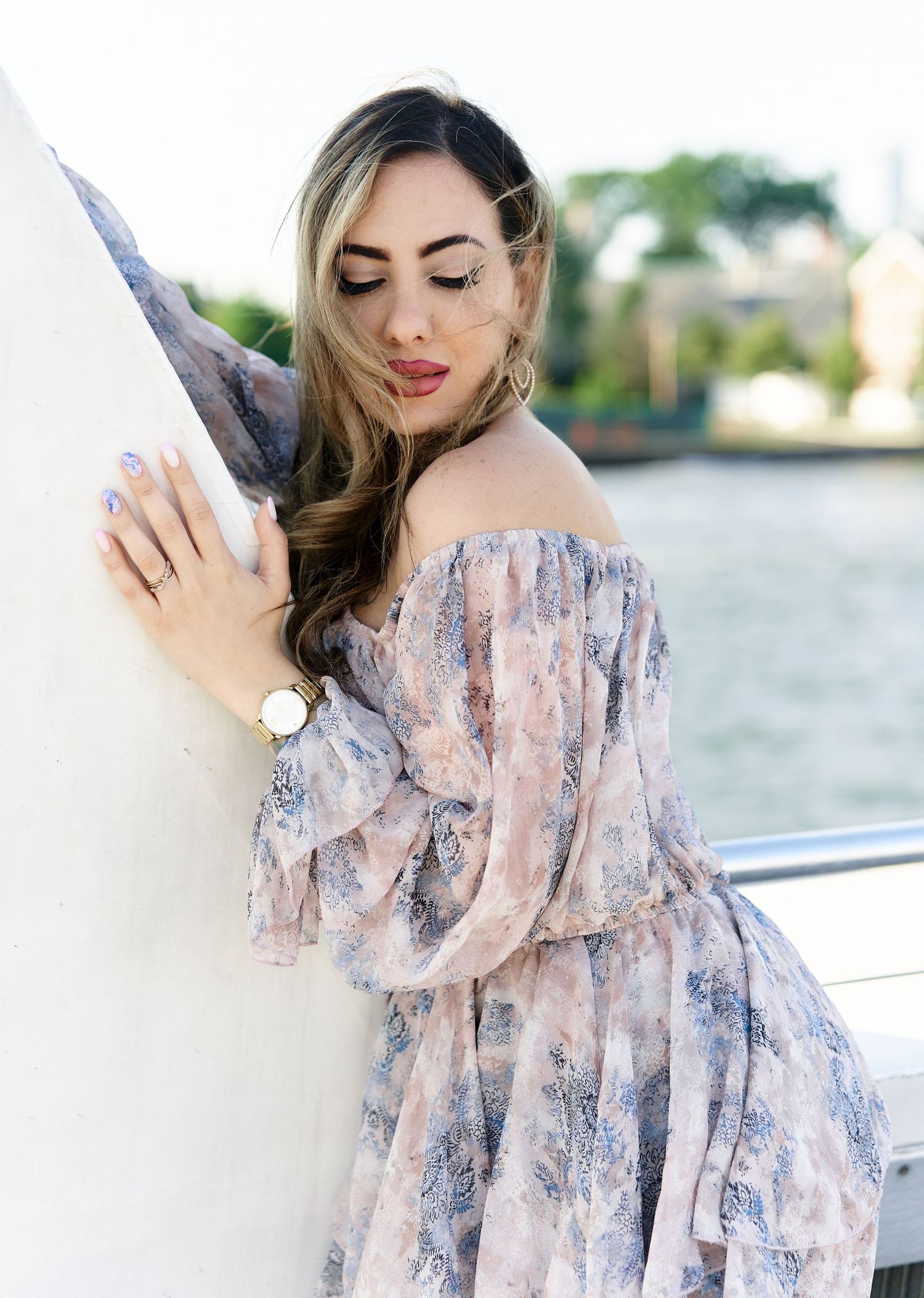 Woman in floral off-shoulder dress posing on a boat with waterfront views.