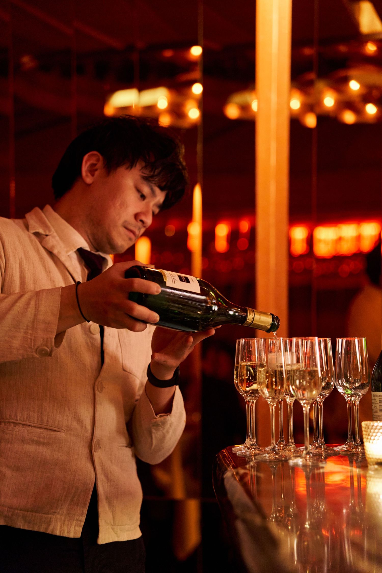 Bartender pours champagne into a row of glasses at a warmly lit bar with golden ambiance.