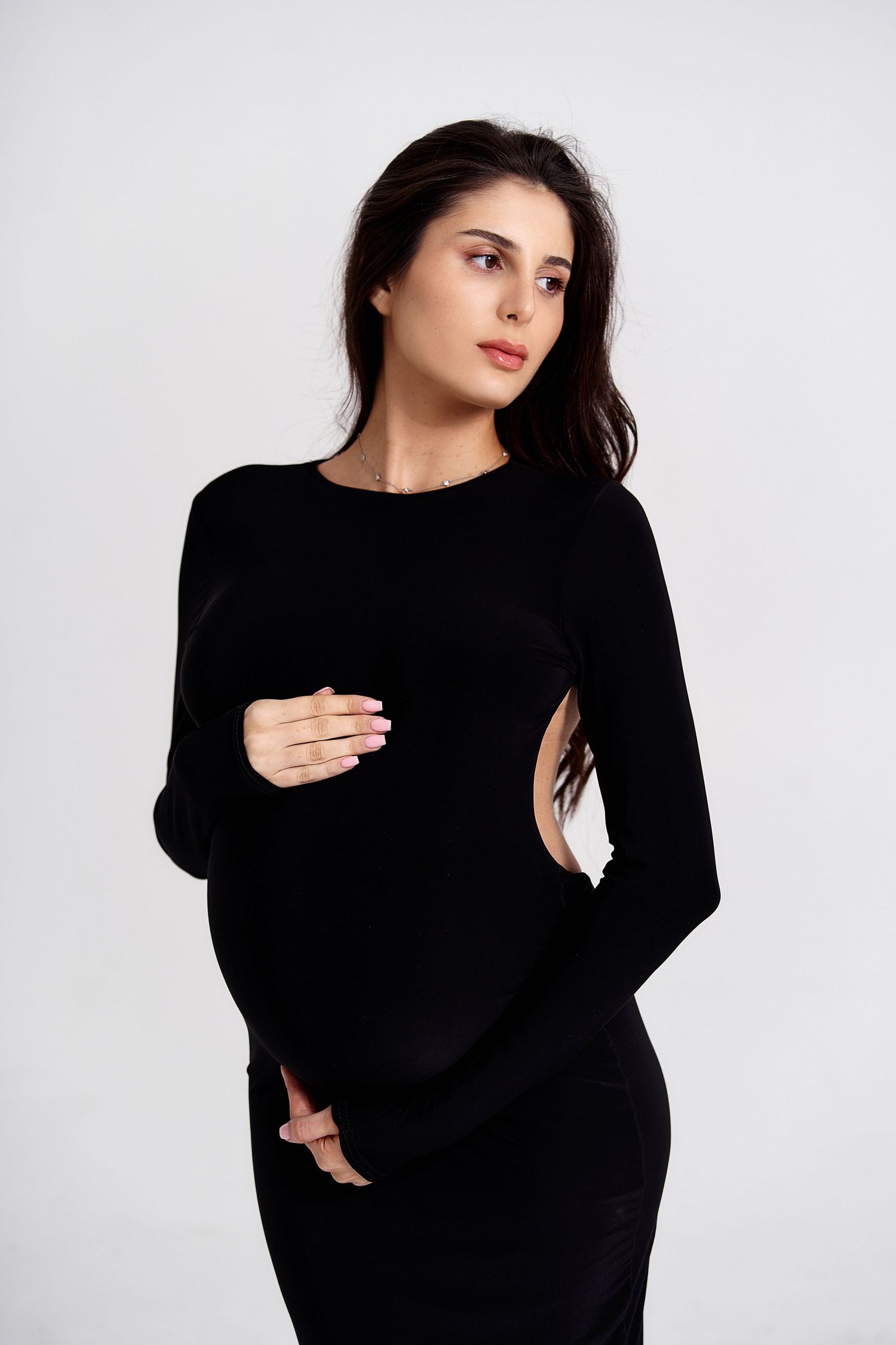 Woman in black long-sleeve cutout dress poses against white studio background.