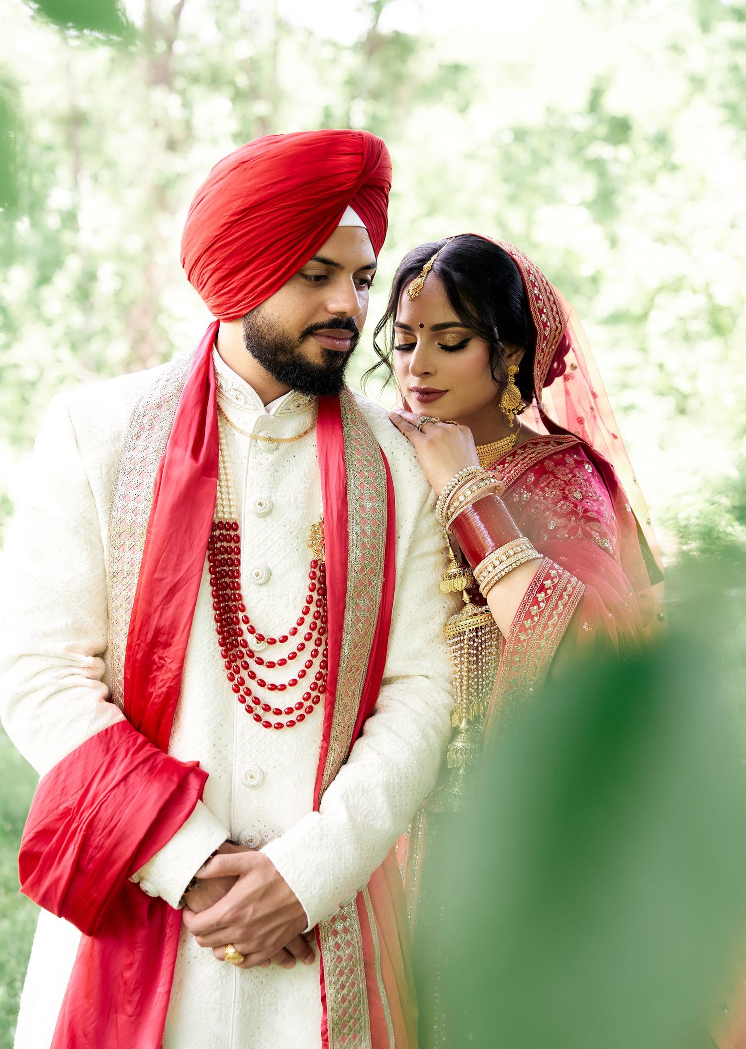 Sikh couple in traditional wedding attire, groom in white sherwani and red turban, bride in red lehenga.