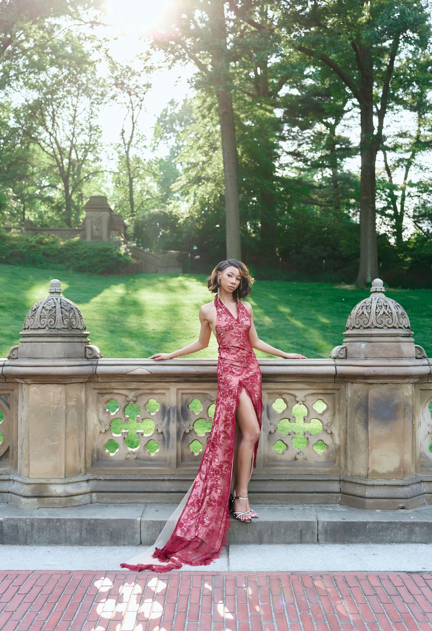 Woman in red lace gown with high slit poses on Bethesda Terrace balustrade in Central Park.