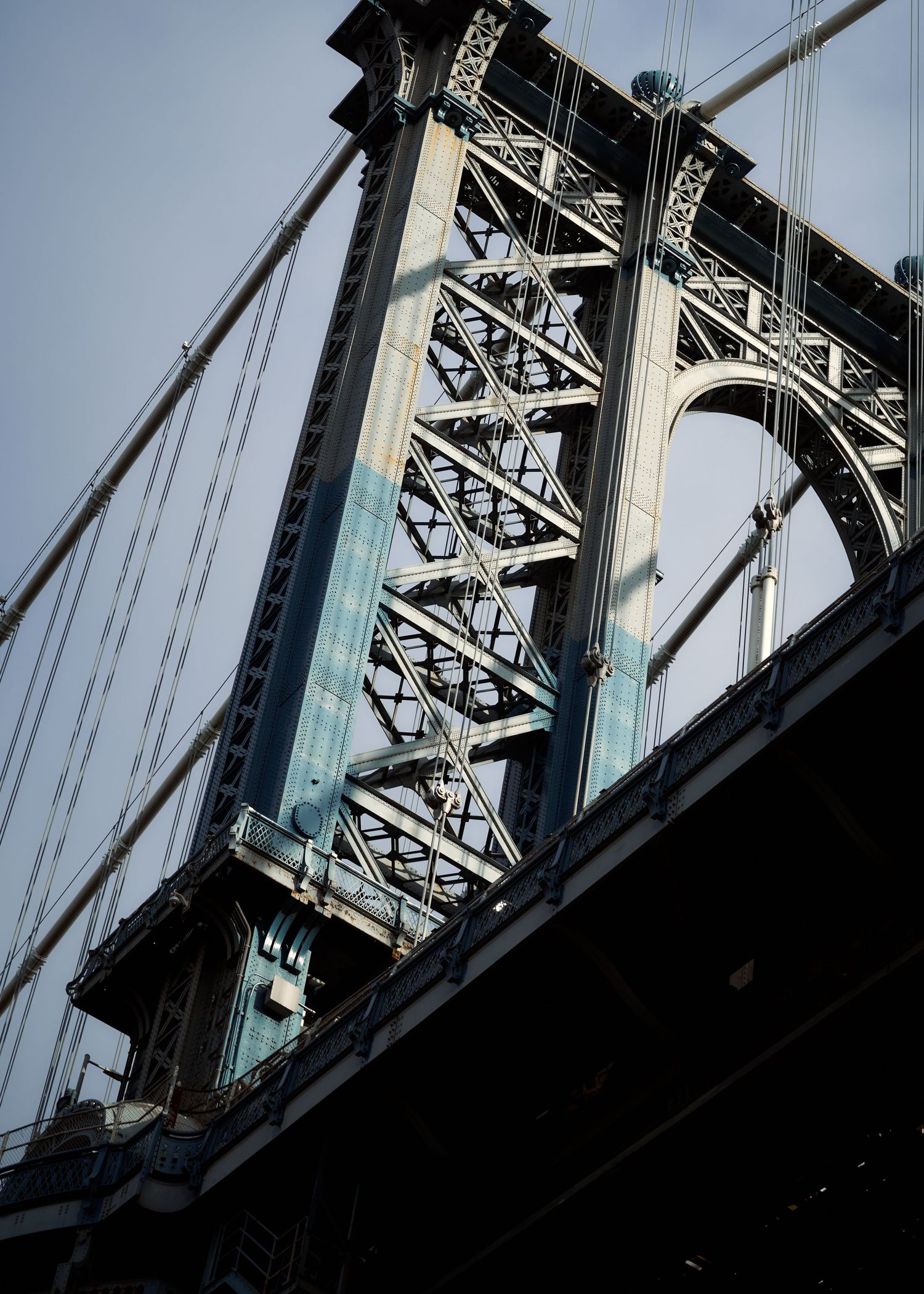 Close-up architectural shot of the Manhattan Bridge steel tower and suspension cables against sky.