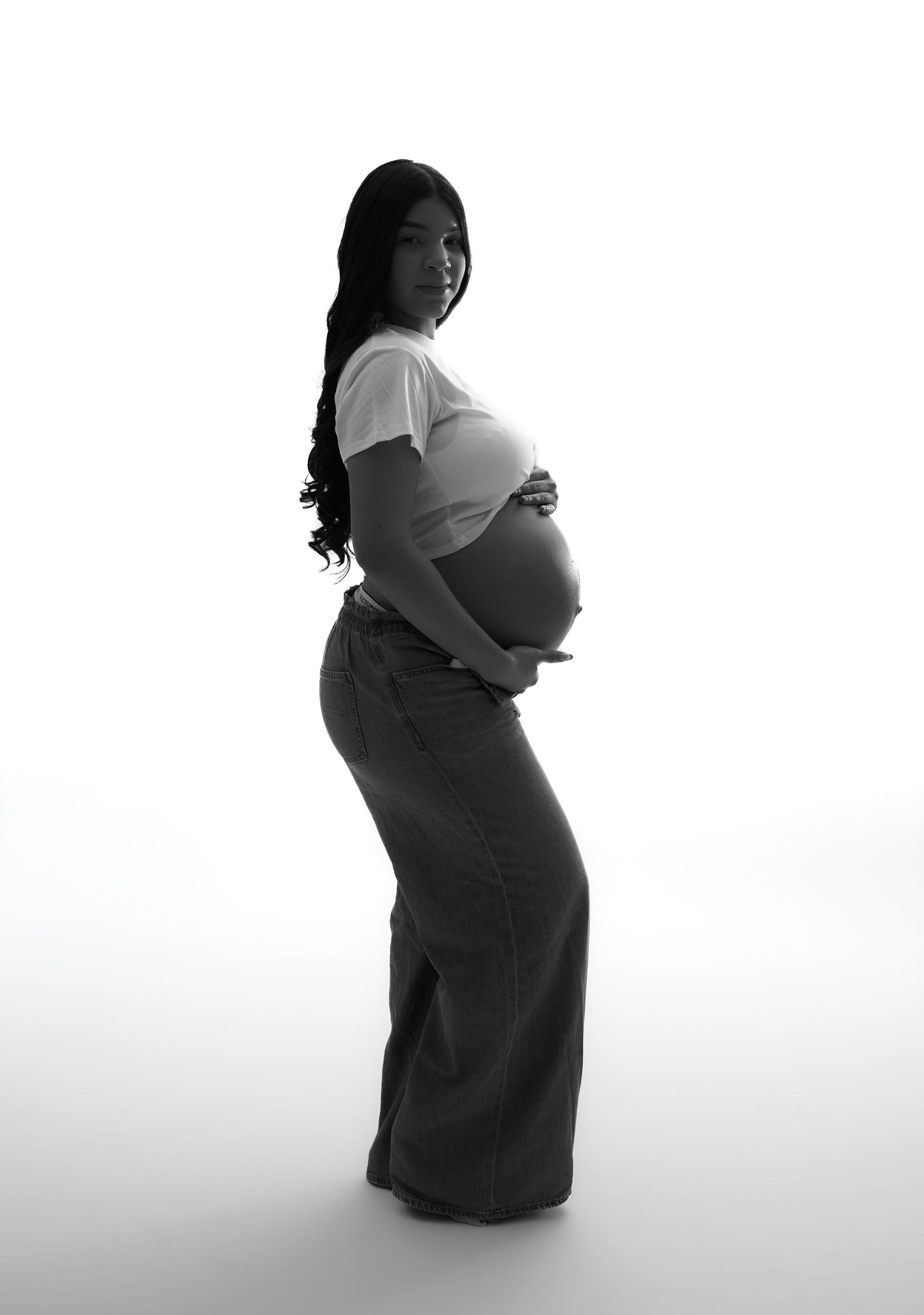 Black and white side profile maternity photo of pregnant woman in white tee and wide-leg jeans.