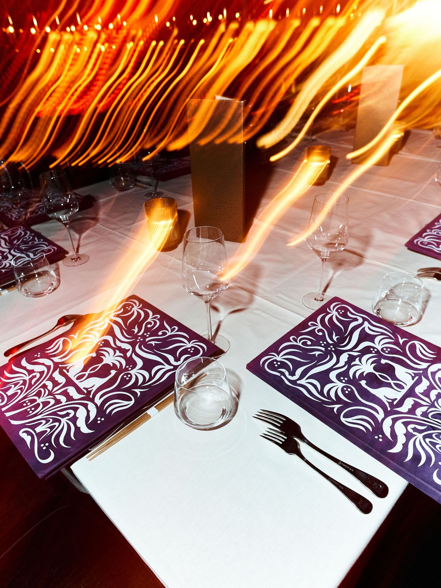 Elegant restaurant table setting with purple placemats and wine glasses with dramatic light streaks overhead.