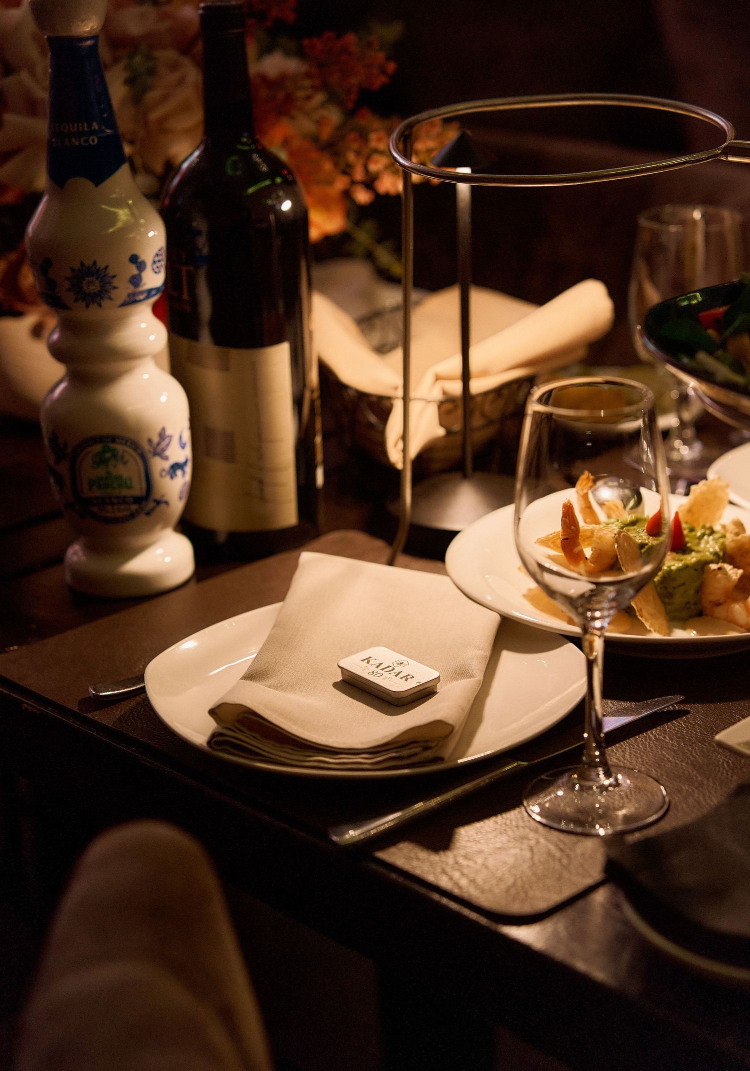 Elegant restaurant place setting with wine glasses, bottles, and plated appetizers in warm lighting.