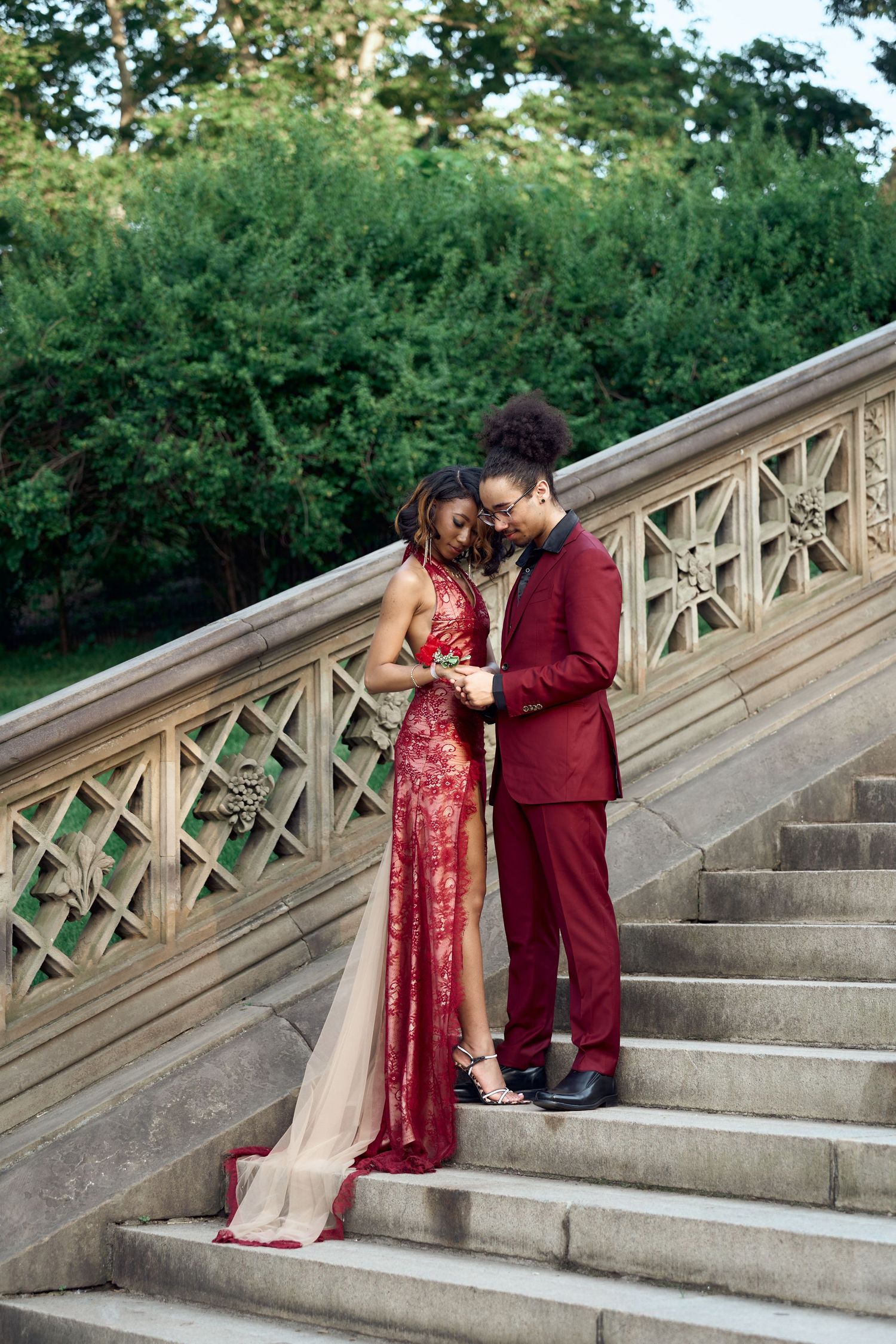 Couple in coordinating red formal outfits stand together on Bethesda Terrace steps in Central Park.