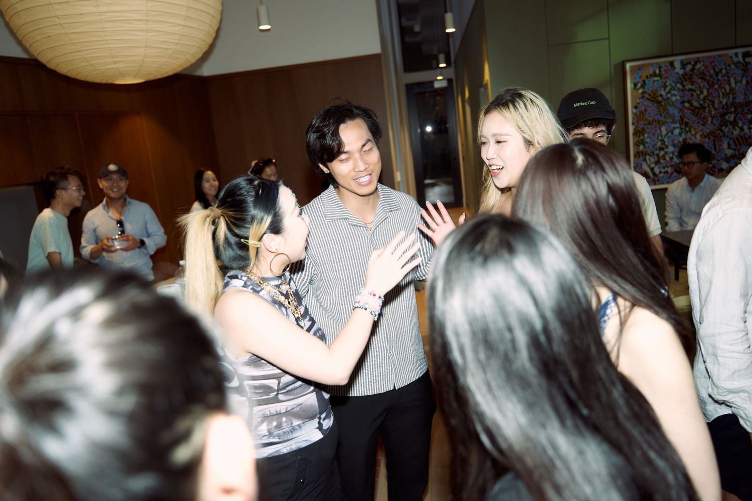 Group of young adults mingle and greet each other warmly at a lively indoor social gathering.