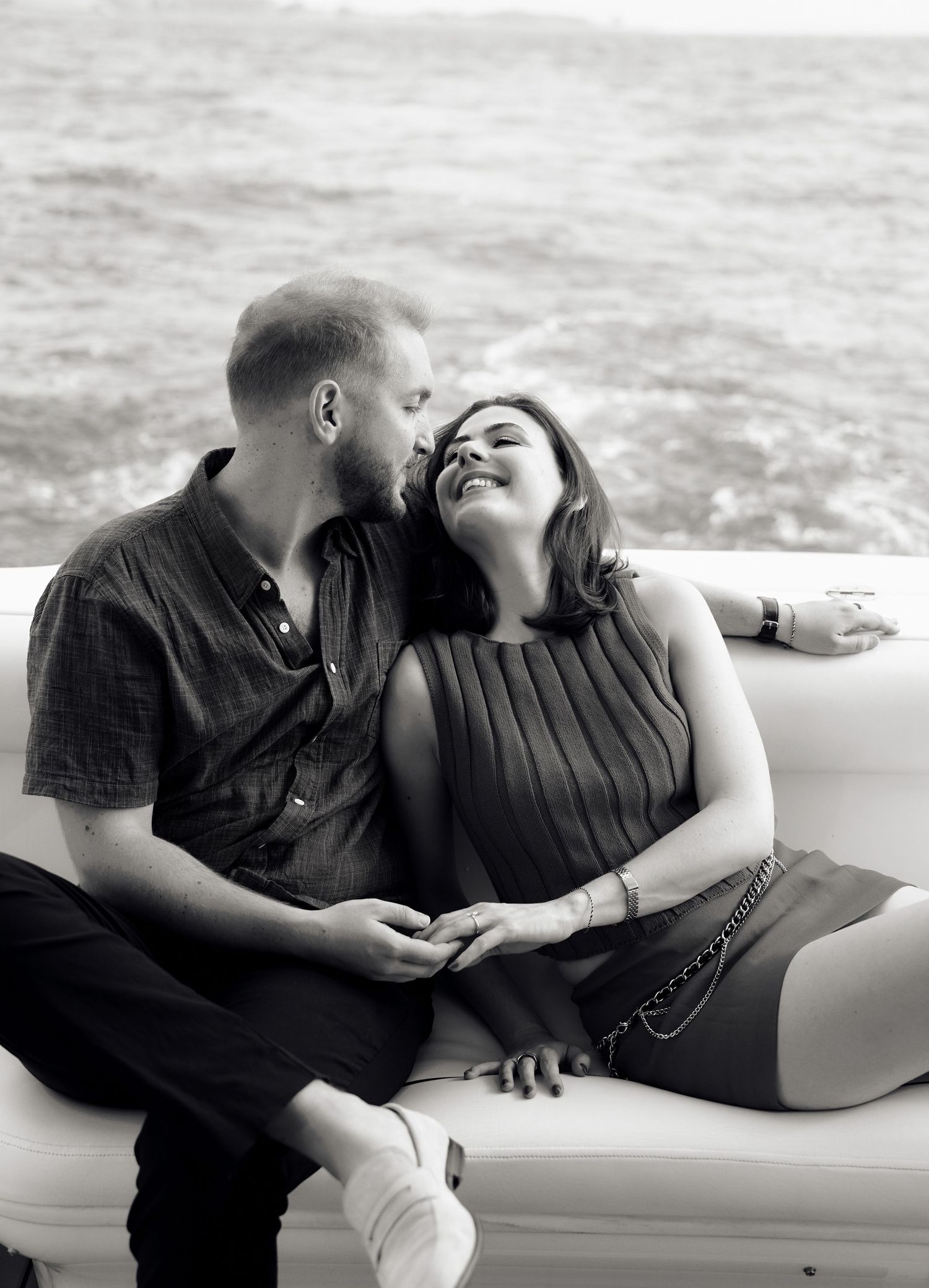 Happy couple laughing together on a white couch aboard a boat, black and white.