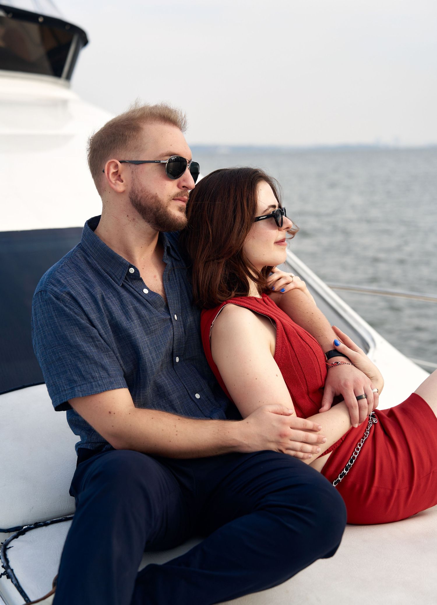 Couple in sunglasses sitting together on yacht deck overlooking calm water.