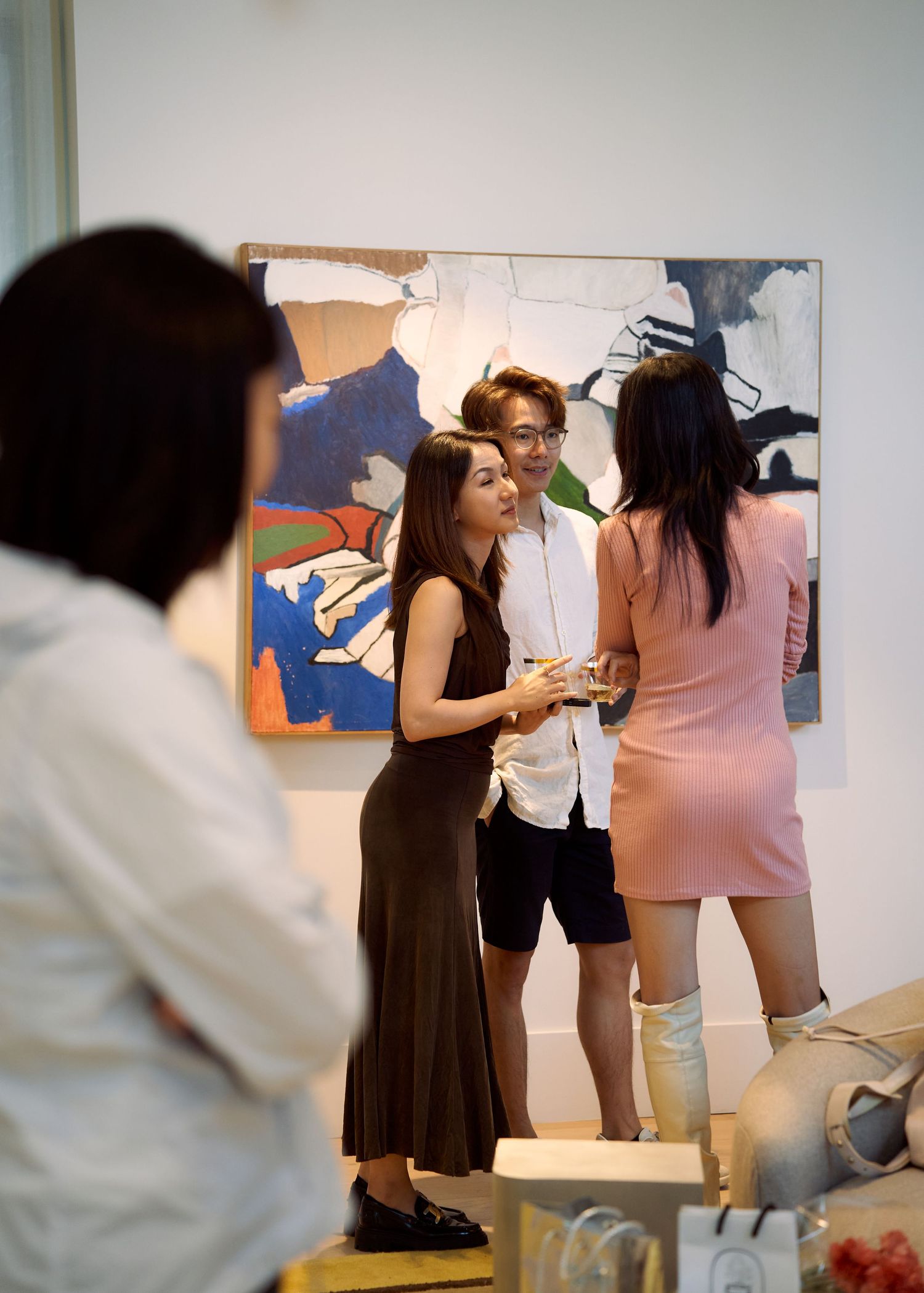 Three guests chat in front of abstract painting at art gallery opening.