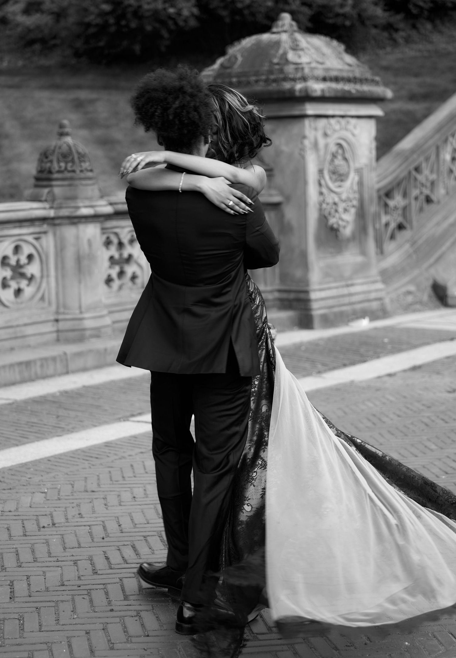 Black and white photo of couple embracing in wedding attire at Bethesda Terrace, Central Park.