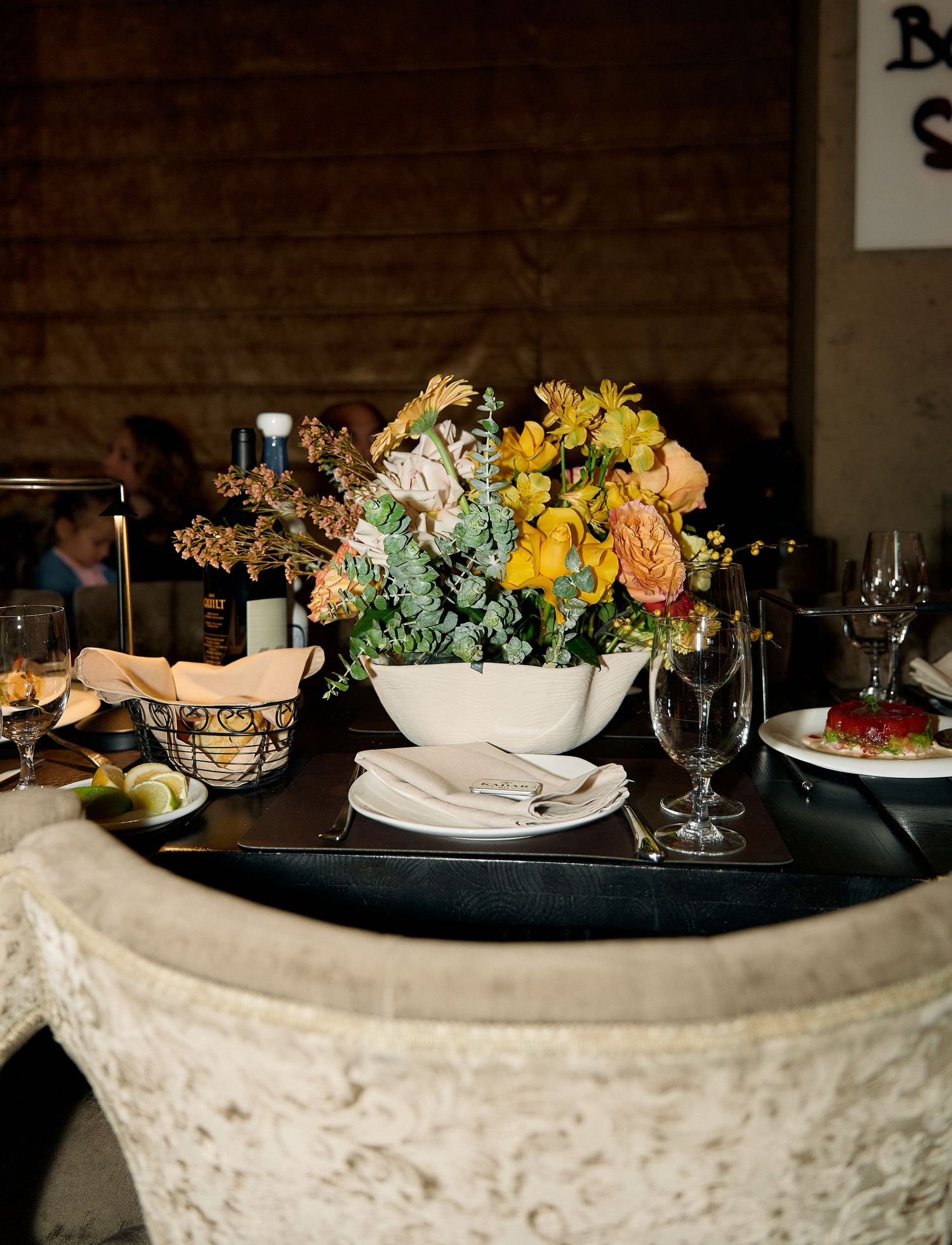 Colorful yellow and peach floral centerpiece in white bowl on decorated event dining table.