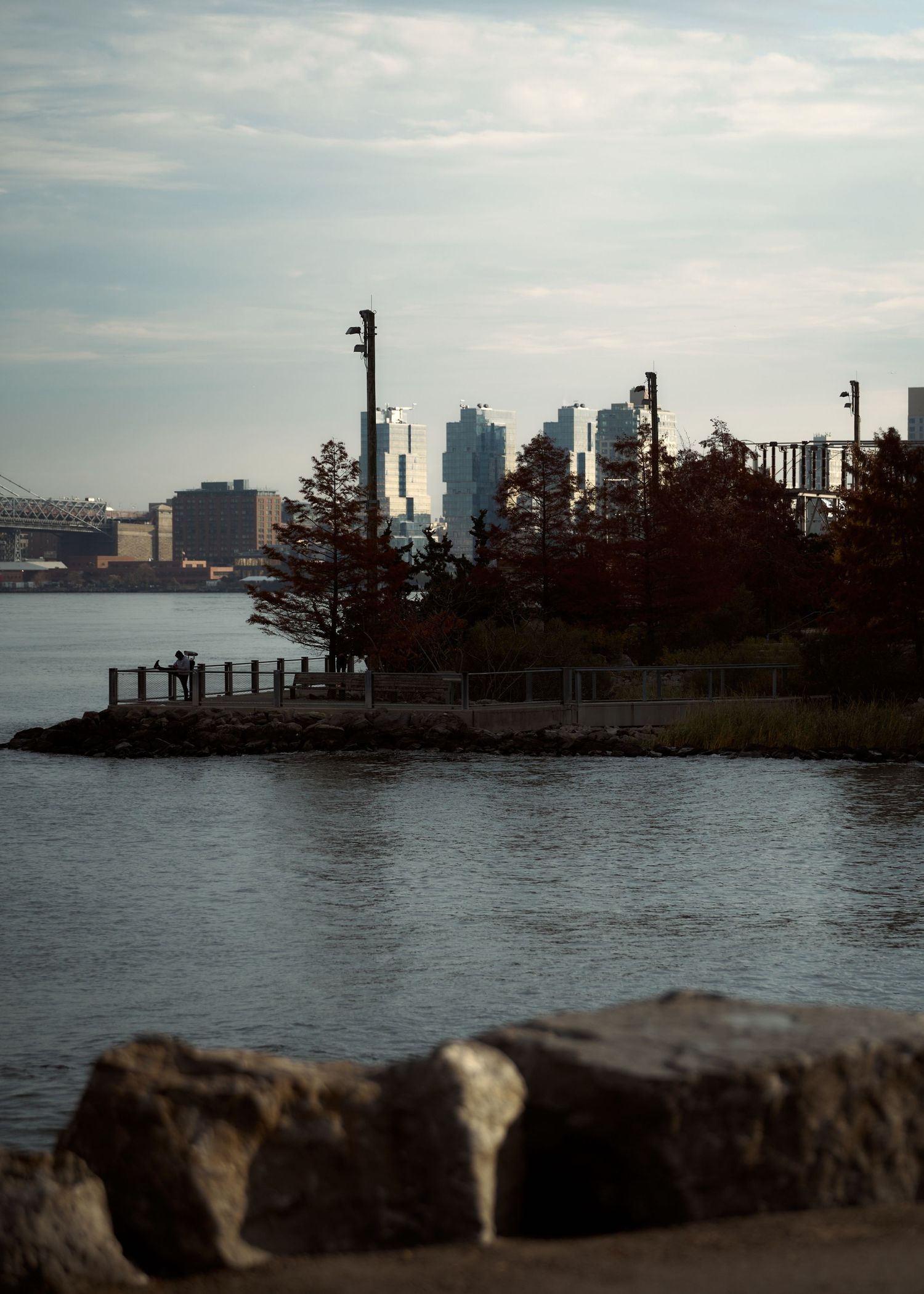 Scenic waterfront view of a small island with autumn trees and the NYC skyline in the background.