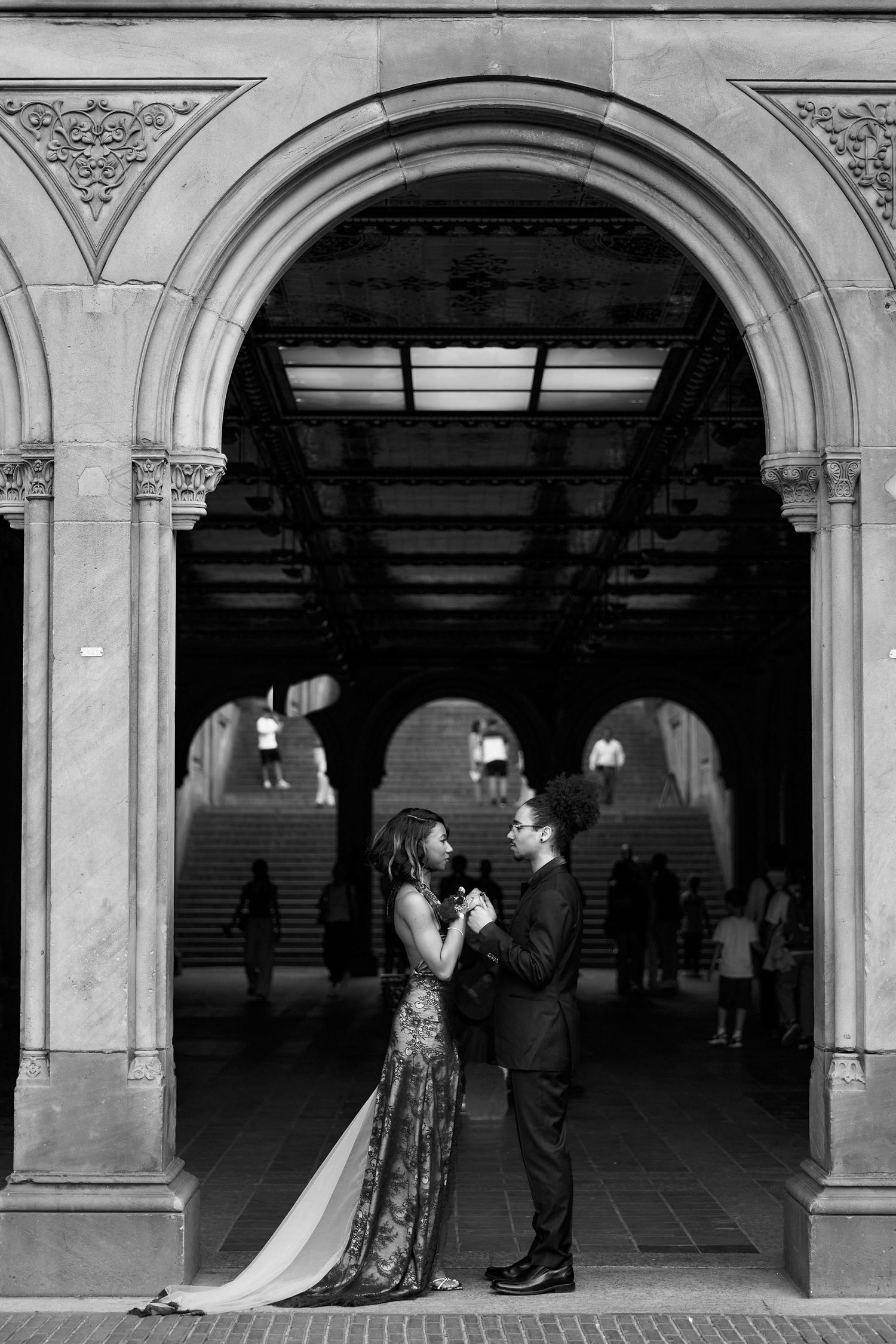 Black and white photo of couple holding hands under Bethesda Terrace archway in Central Park.