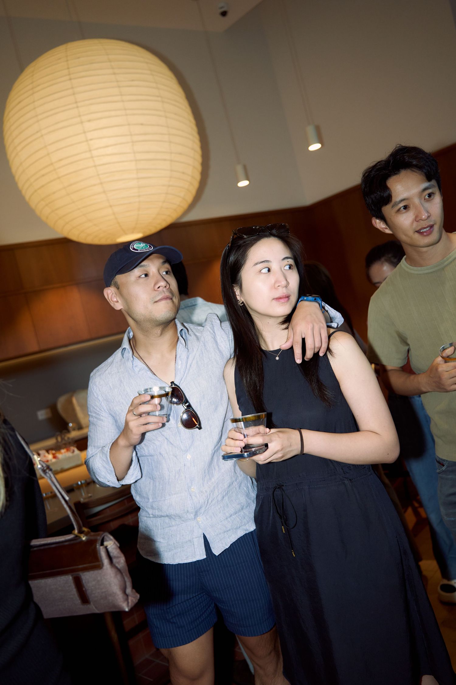 Couple holding drinks looks attentively across the room at a relaxed indoor social event.