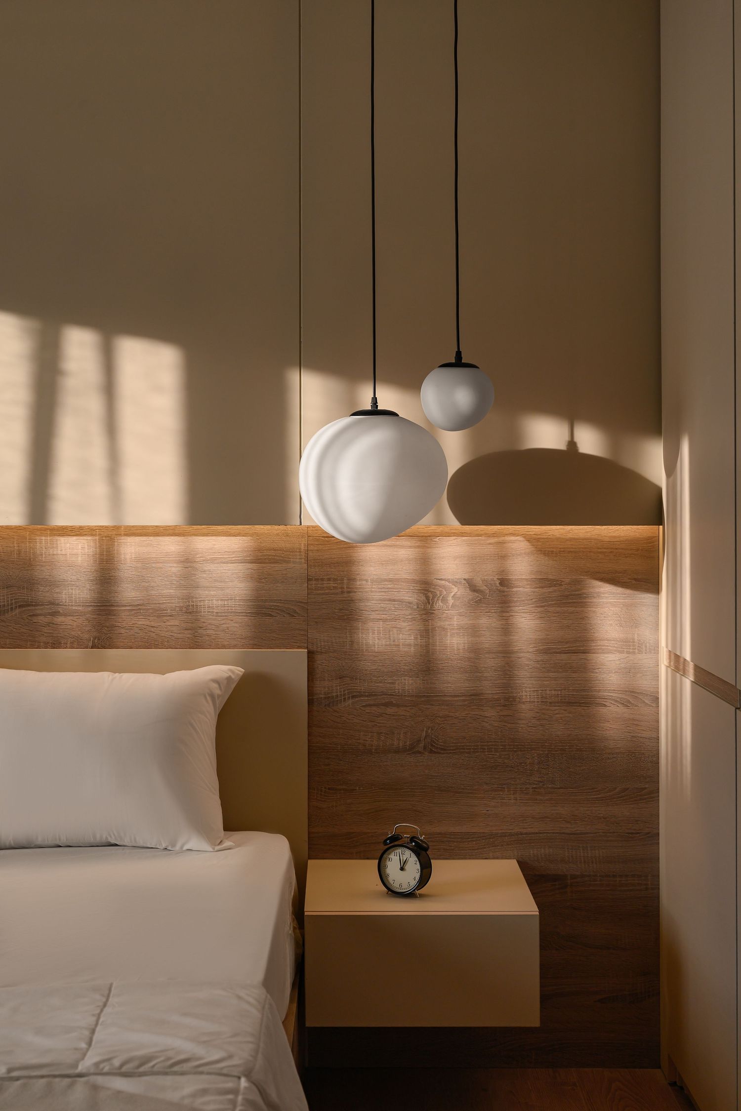 Minimalist bedroom corner with spherical pendant lights and wooden headboard detail. Interior Photography
