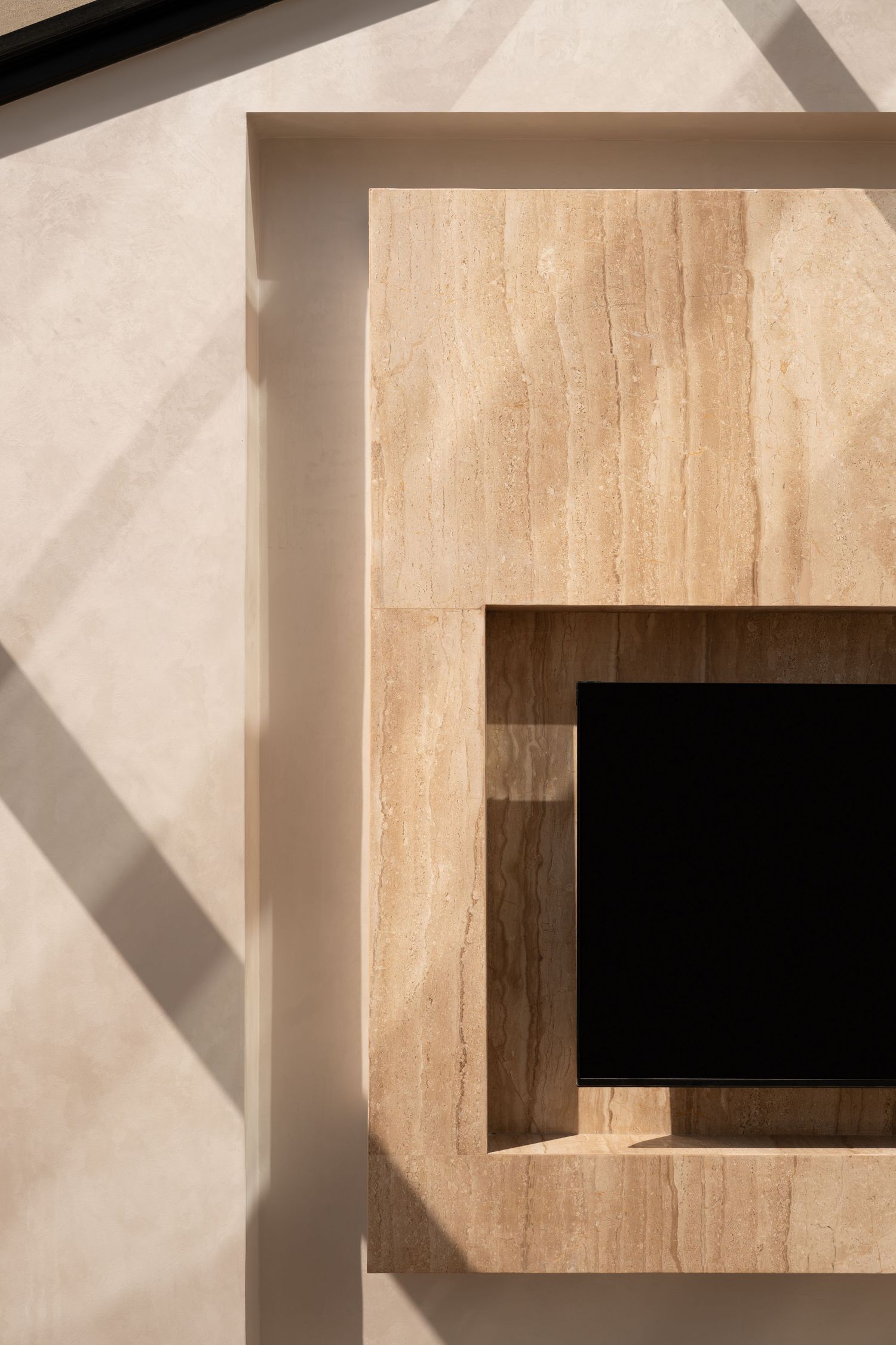 Aerial view of a travertine marble fireplace surround with dark opening, casting geometric shadows on beige wall.