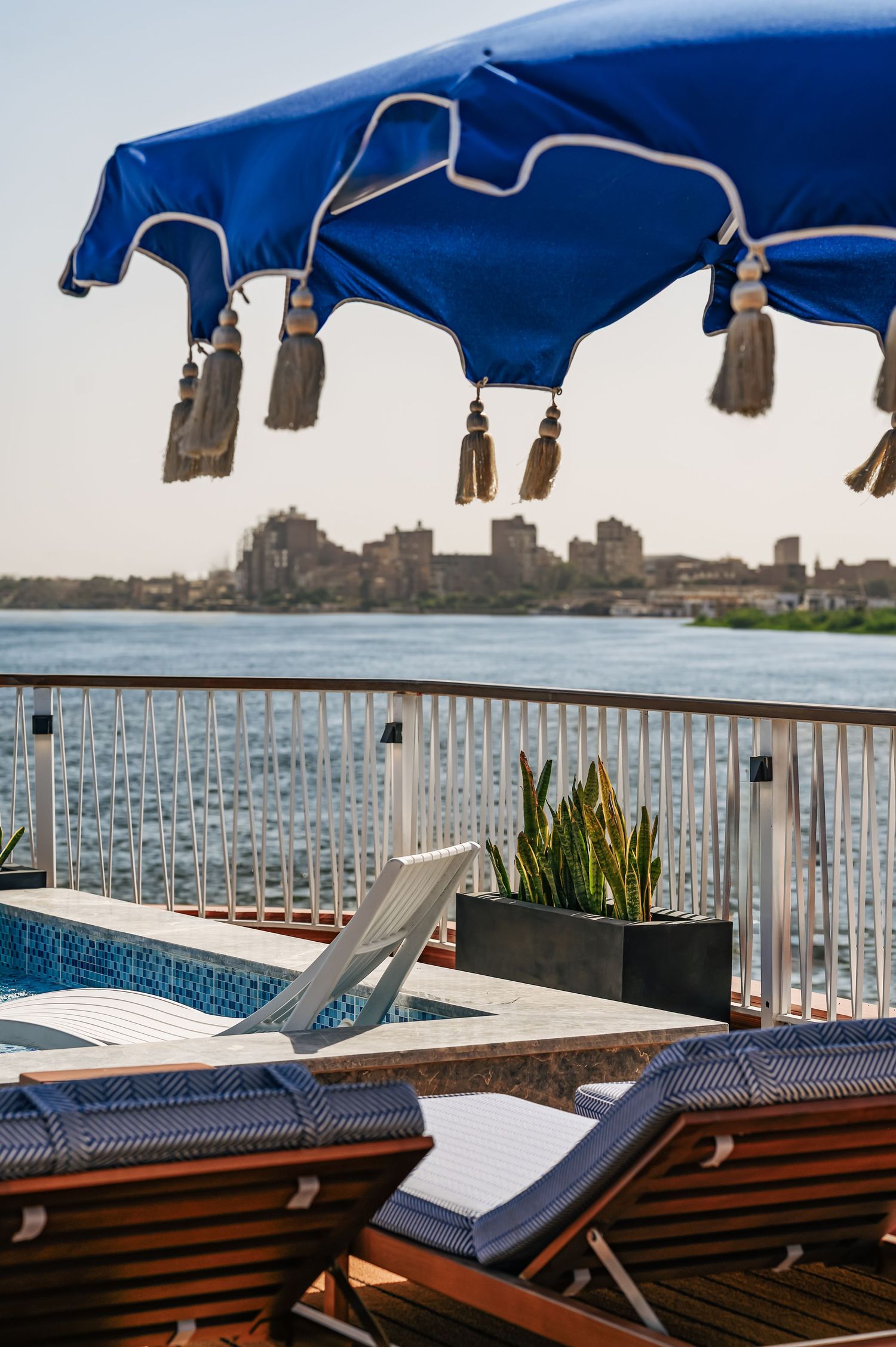 Pool deck loungers with blue umbrellas overlooking waterfront skyline. Interior Photography