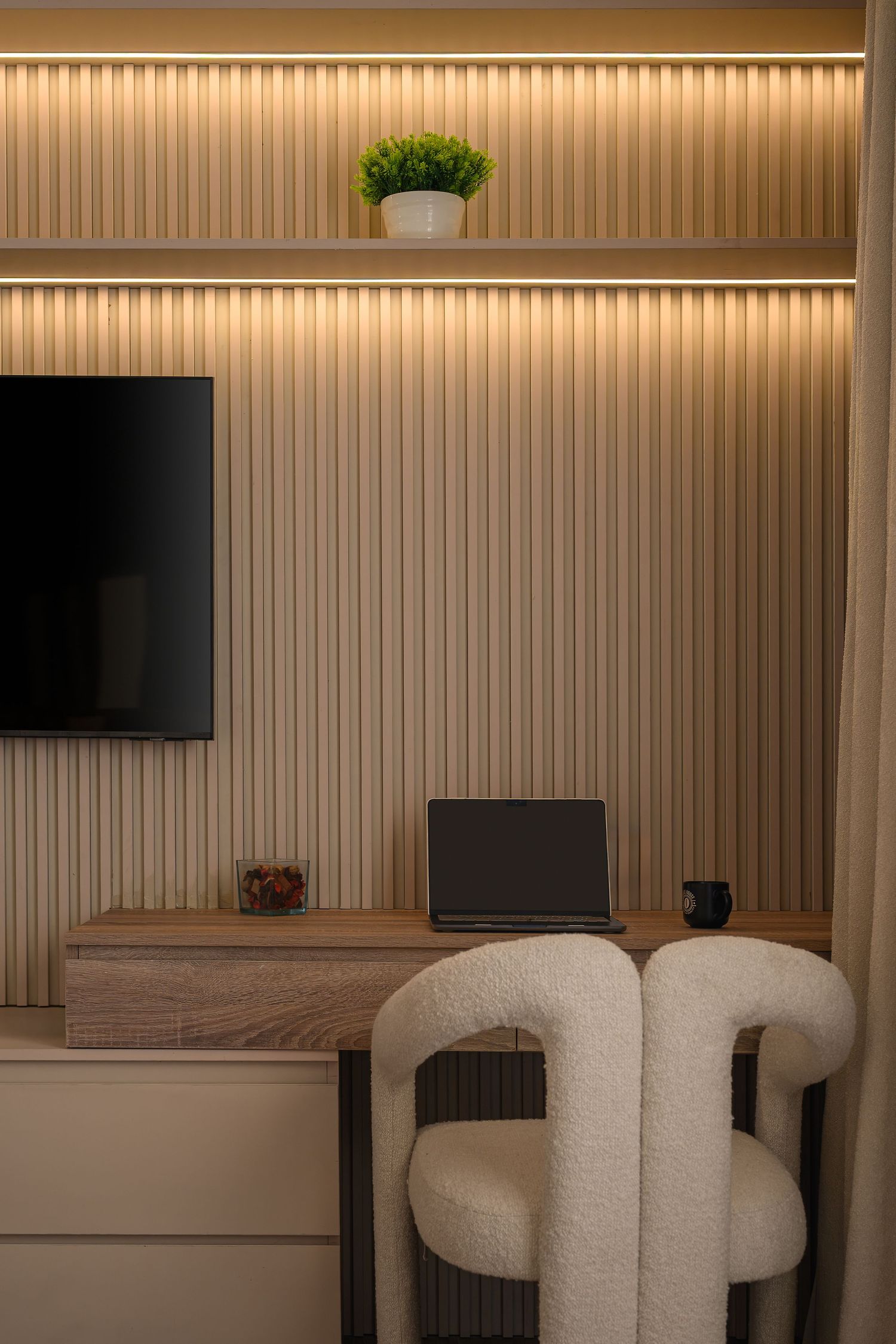 Home office nook with textured wall panels, mounted TV, and plush white chair. Interior Photography
