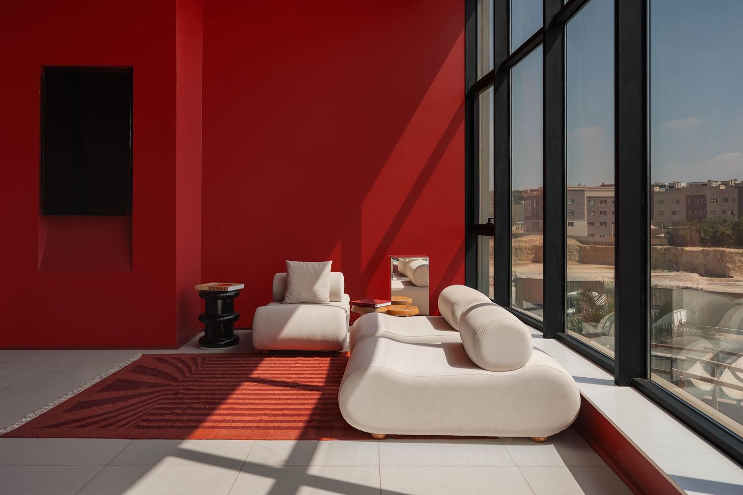Modern living space with white sofa against red walls and large windows offering city views. Interior Photography