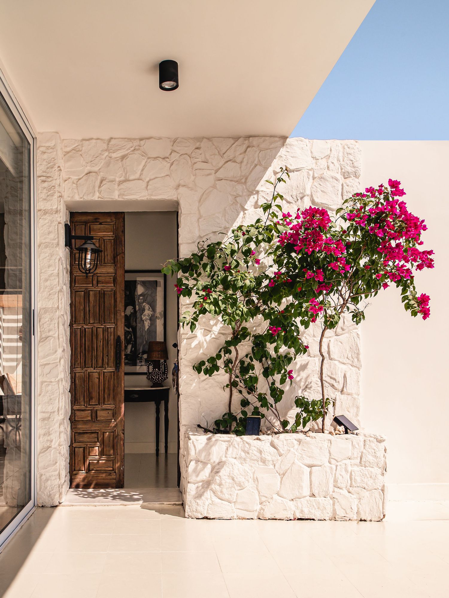 White stone exterior entrance with wooden door and vibrant pink bougainvillea flowers. Interior Photography