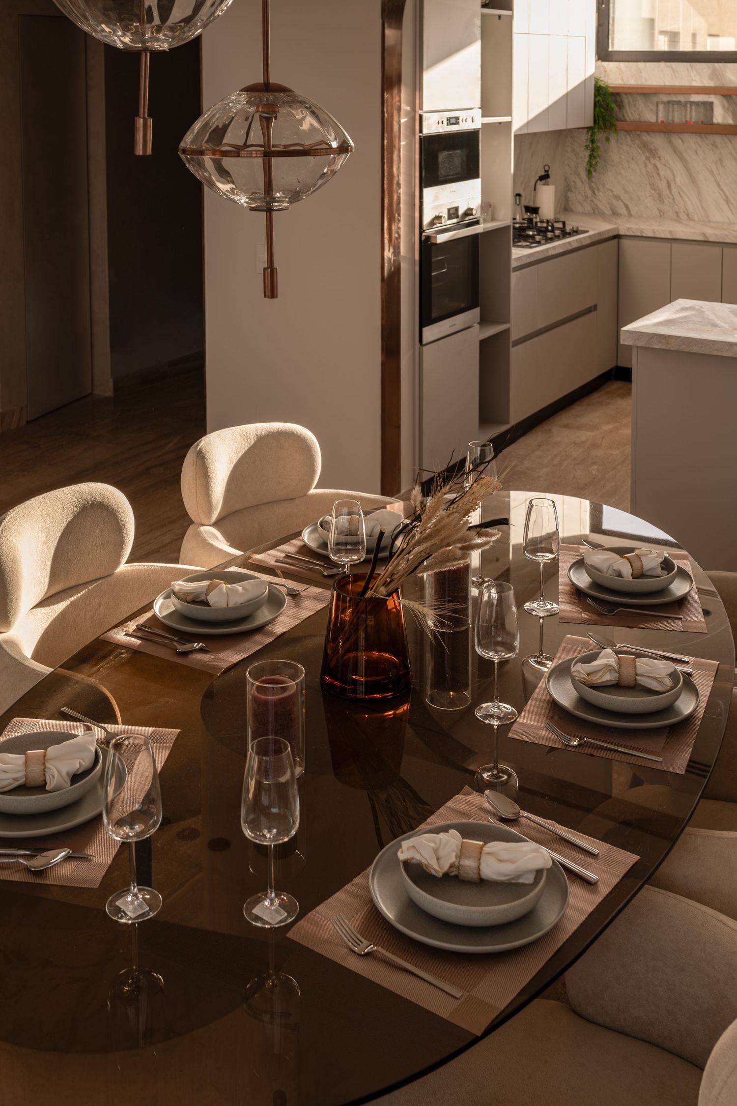 Elegant dining table set with wine glasses, plates, and amber vase centerpiece in a modern open-plan kitchen.