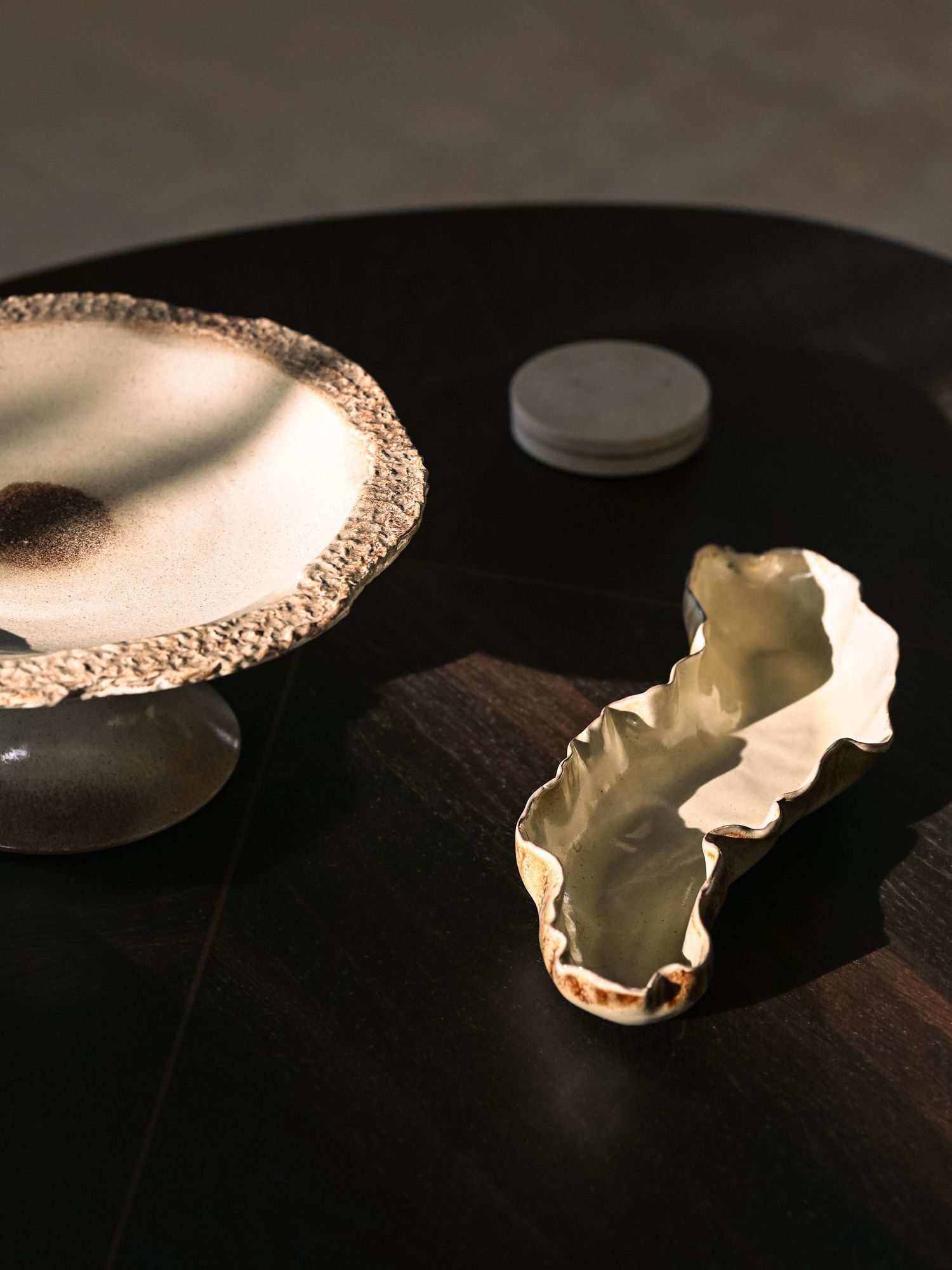 Gold-rimmed ceramic cake stand and organic-shaped gold dish displayed on a dark wooden table.