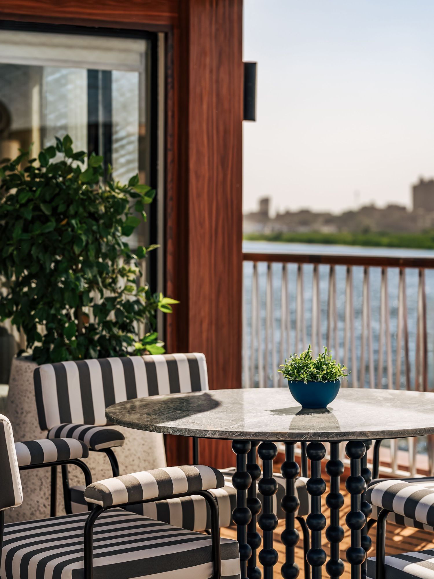 Elegant patio seating area with striped cushions and white tables overlooking water. Interior Photography
