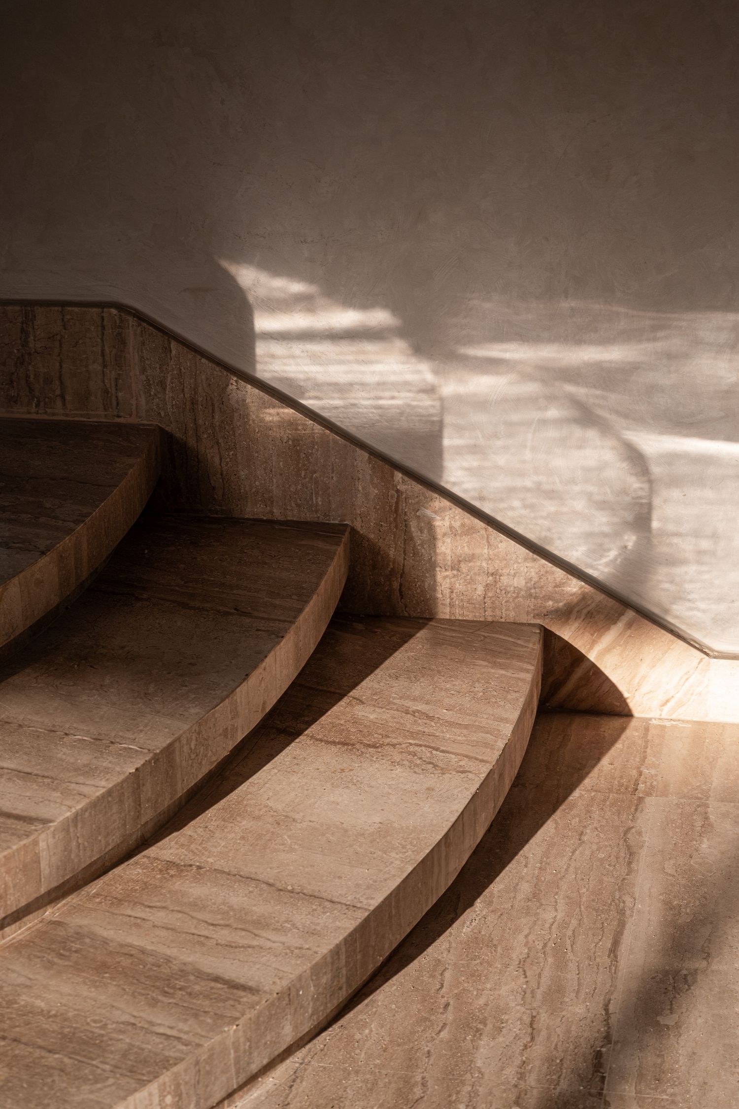 Curved travertine marble staircase with soft natural light casting elegant shadows on smooth stone steps.