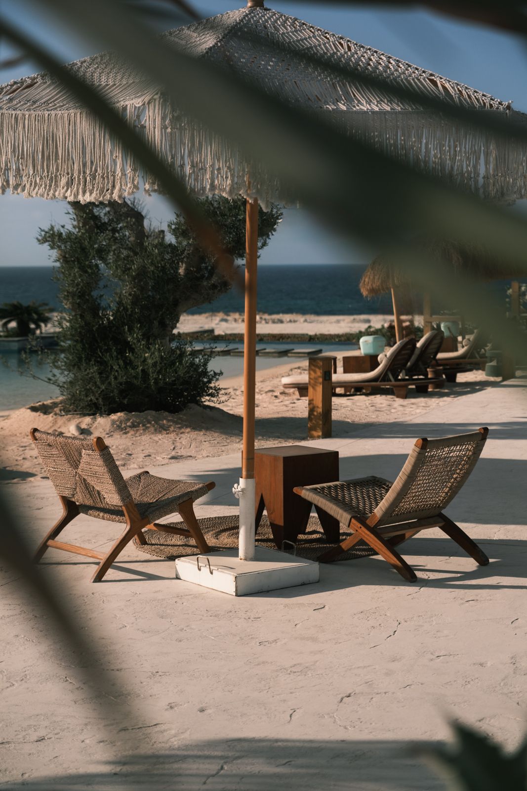 Beach lounge chairs arranged on white sand with ocean views under natural woven umbrellas. Interior Photography