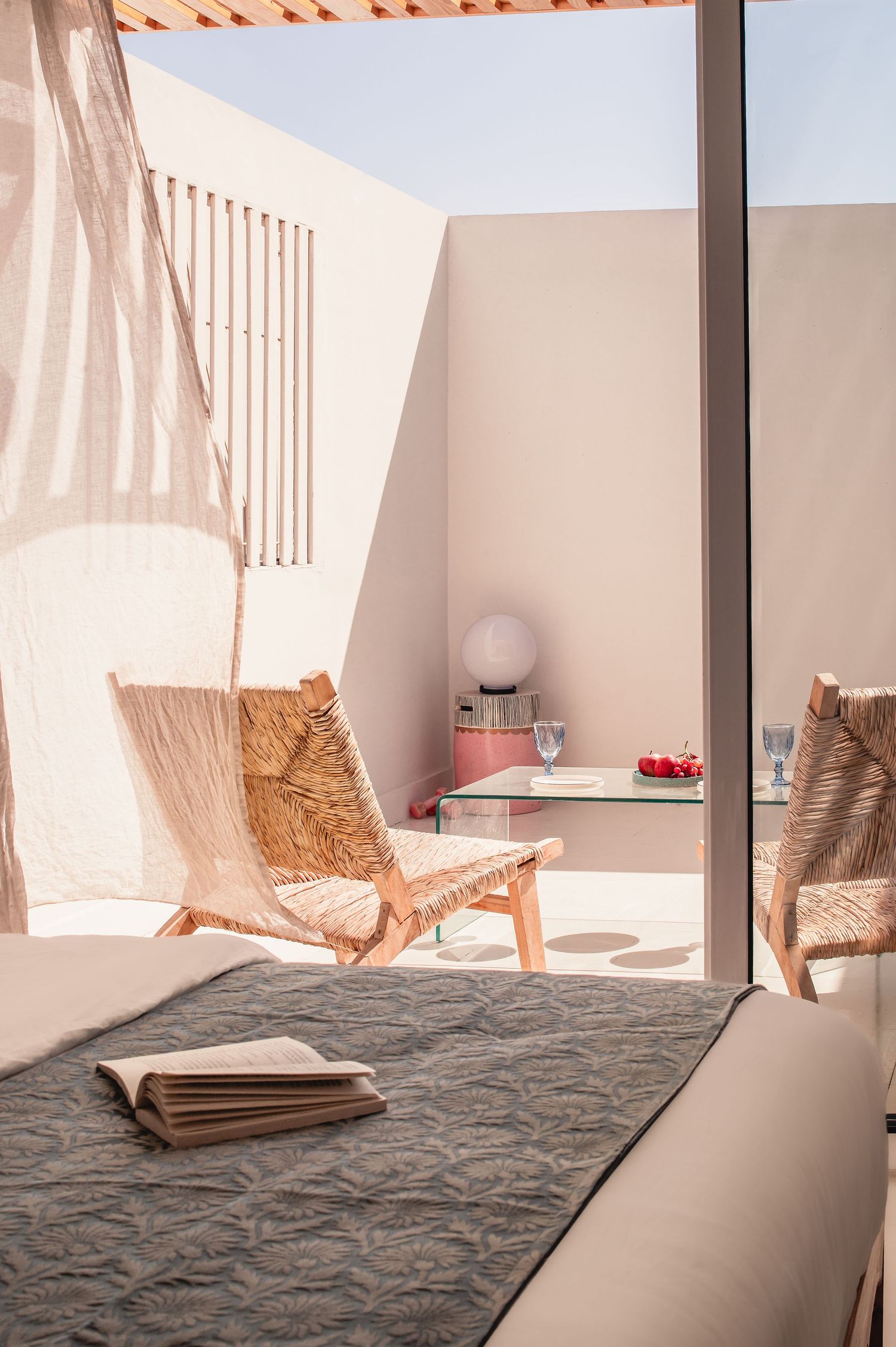 Sunlit bedroom with woven chairs and geometric shadows on white walls. Interior Photography