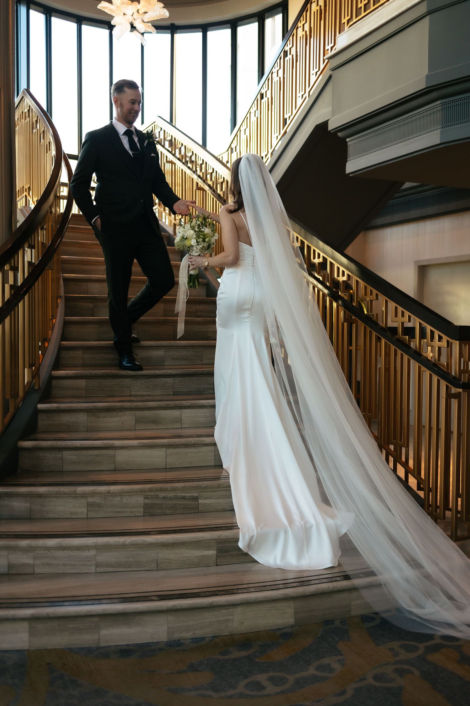 Elegant wedding couple posing on a grand curved staircase with ornate gold railings.