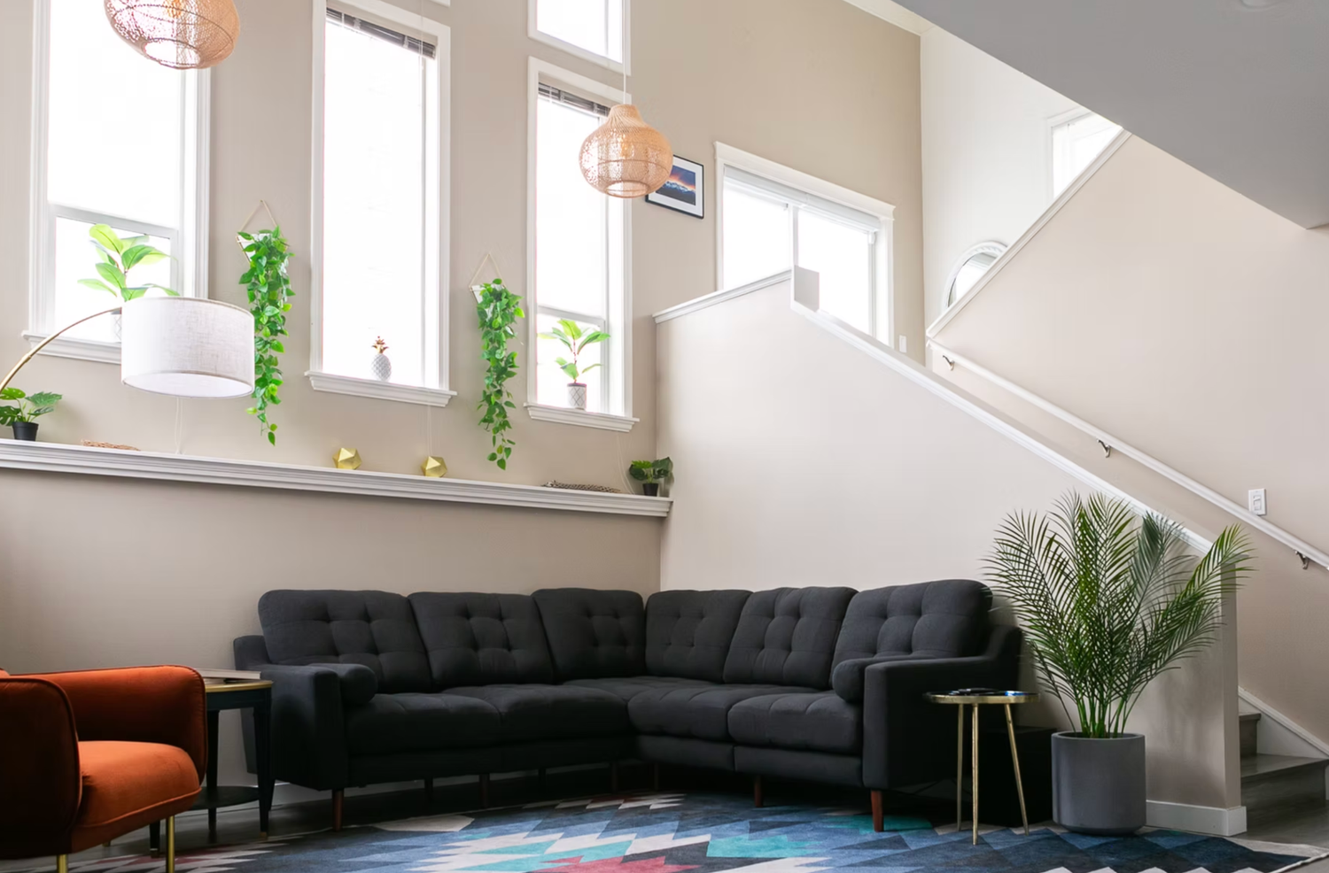 Modern office lounge area with grey sectional sofa, orange accent chair, and natural light from clerestory windows.