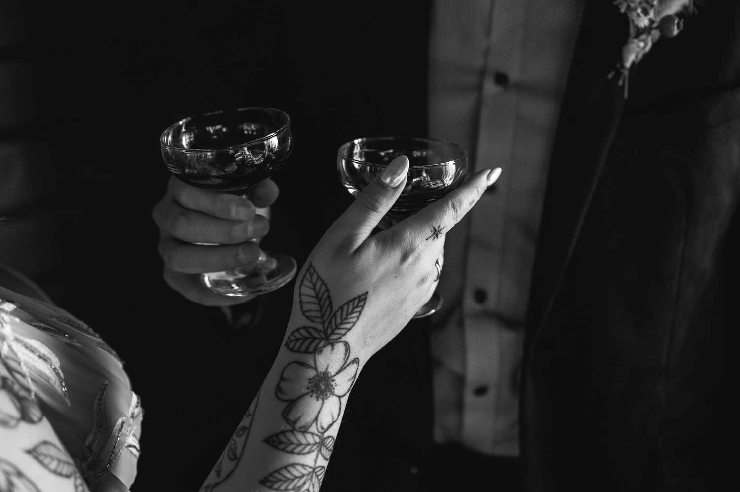 Tattooed hands holding drinks in a dimly lit setting creating a moody atmosphere.
