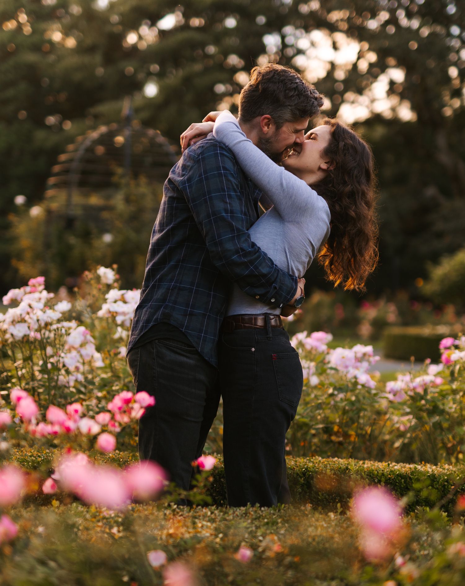 Couple sharing passionate embrace among pink flowers in sunset garden.