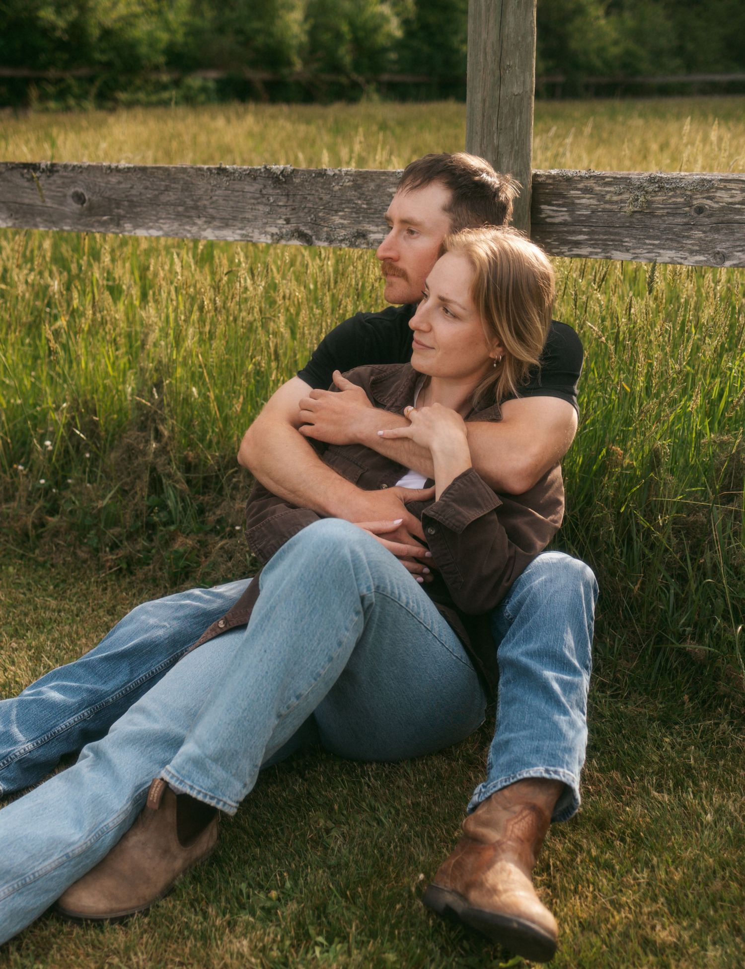 A couple relaxes together on grass during a warm summer evening in casual denim and brown attire.