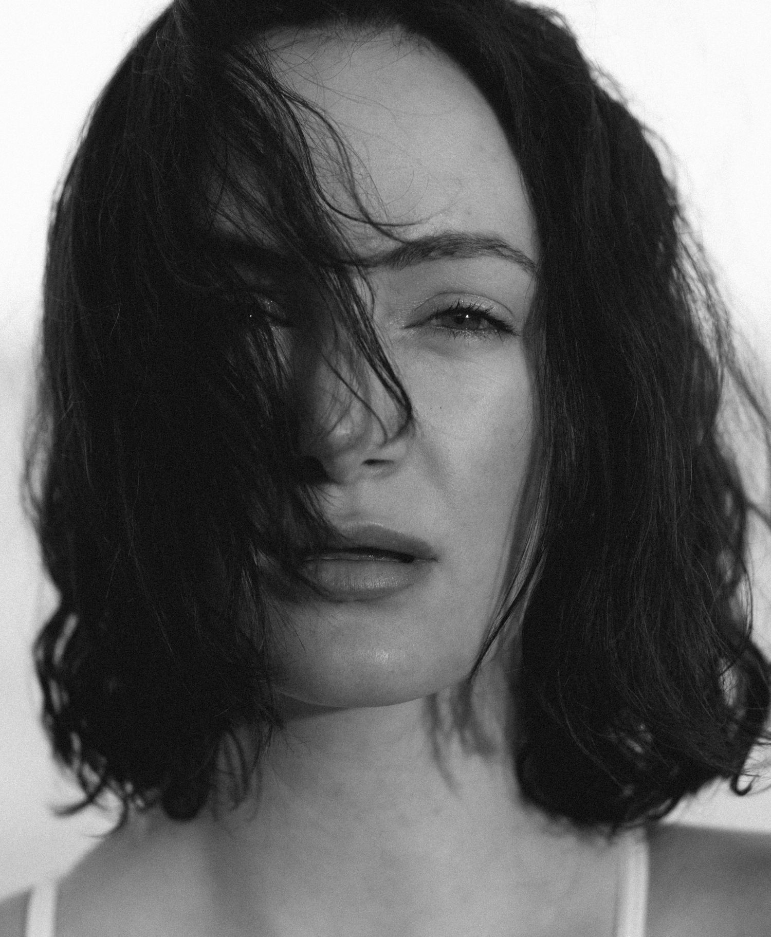 Dramatic black and white portrait with windswept hair against white background.