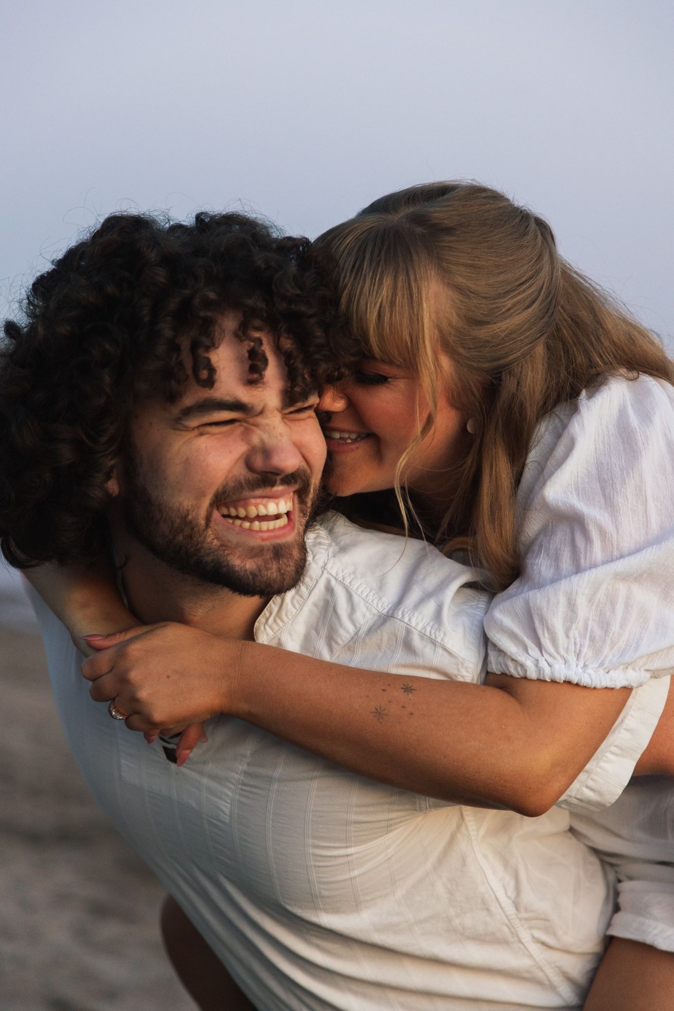 Joyful couple sharing playful piggyback moment on beach at sunset.
