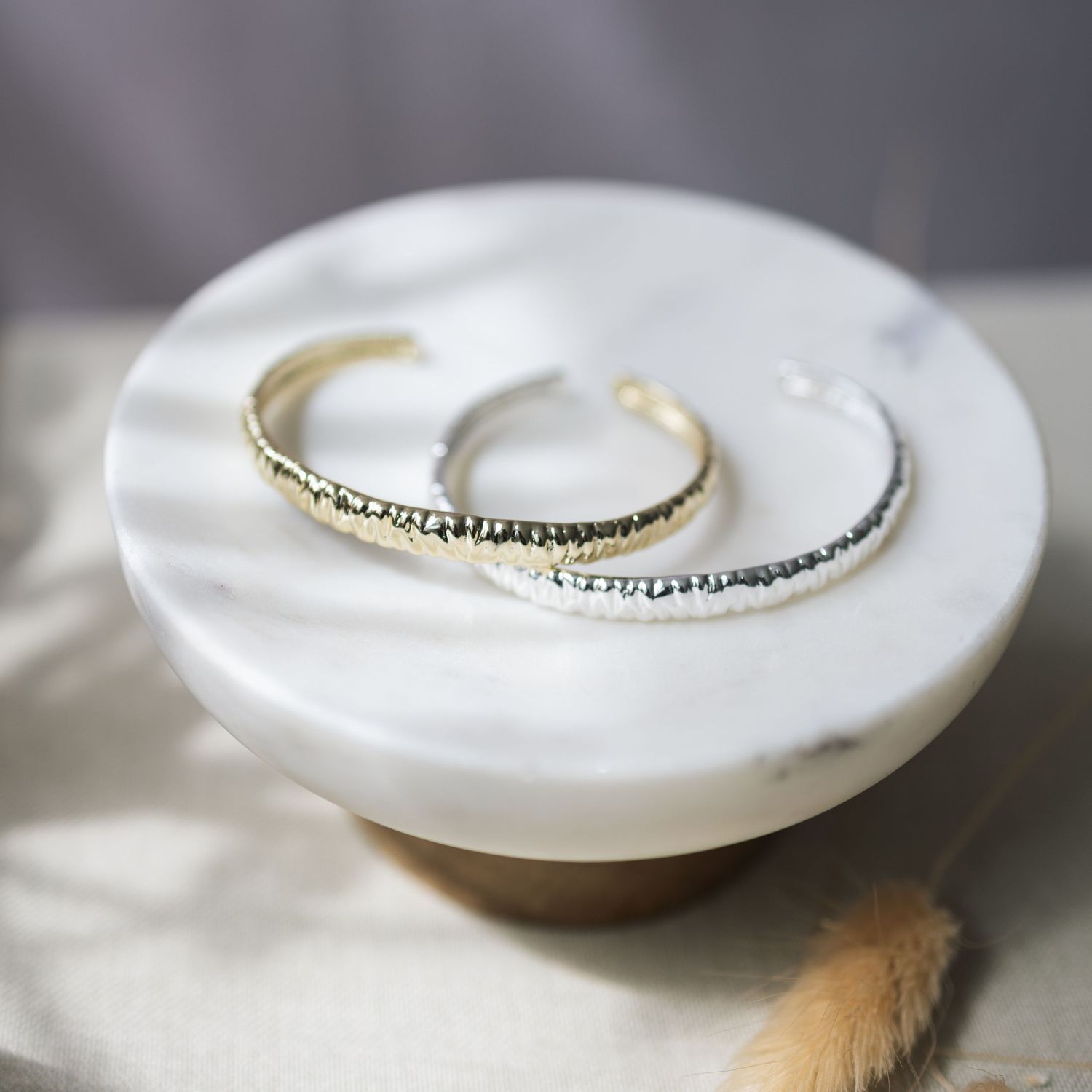 Delicate silver and gold rings with gemstones displayed on a white marble surface in soft natural lighting.