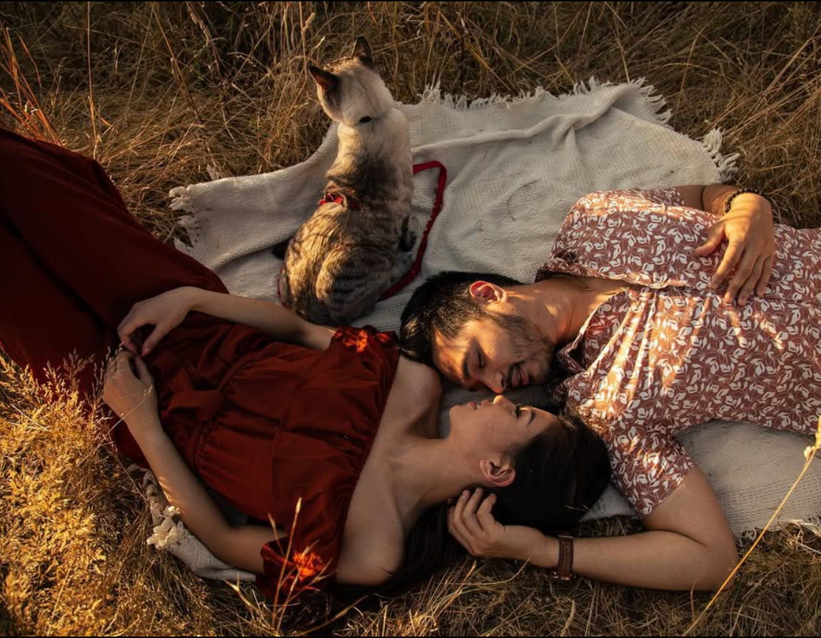 Two people laying on a blanket outdoors with decorative lighting in a romantic setting.