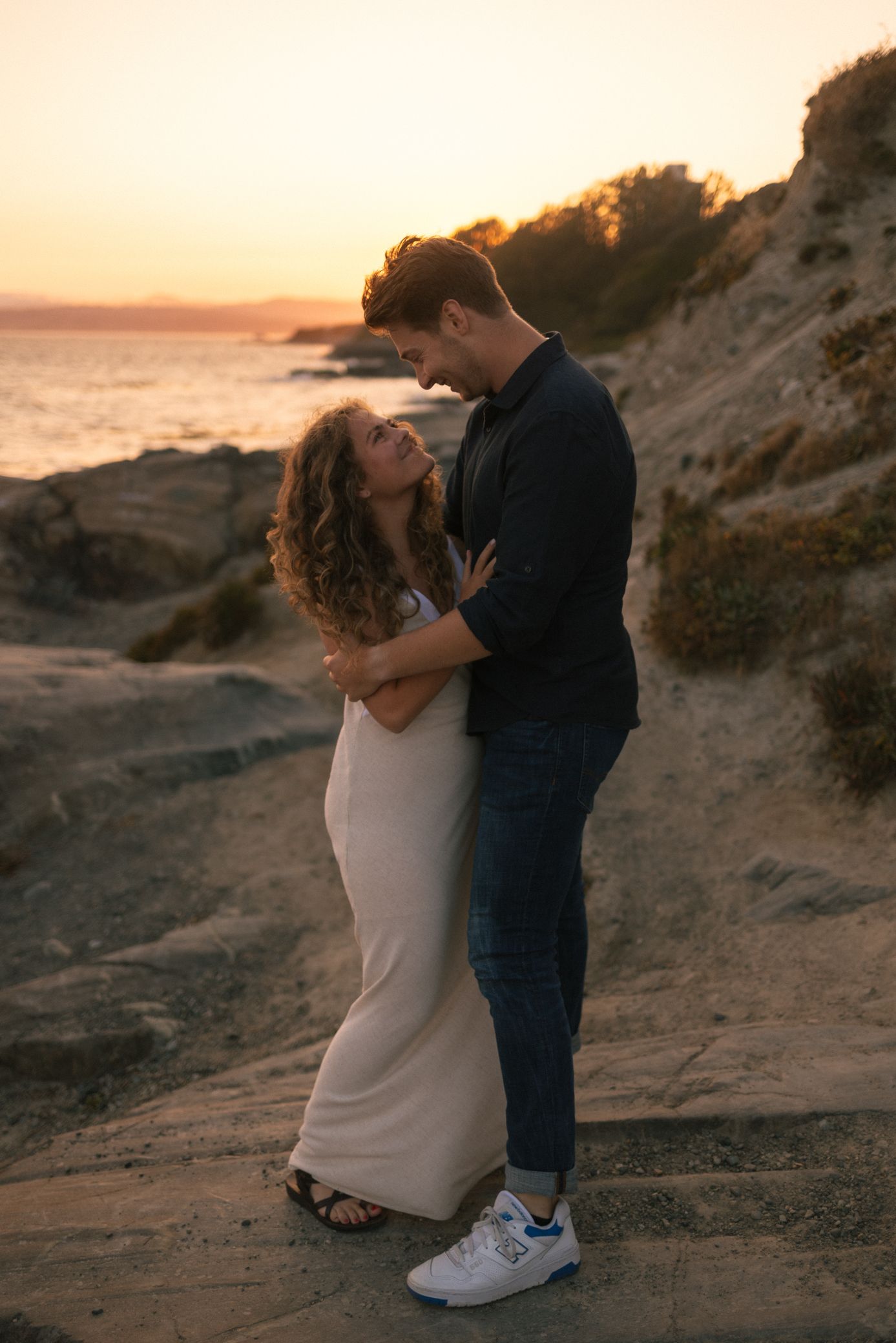 Romantic couple shares intimate moment on coastal cliffs during golden hour sunset.