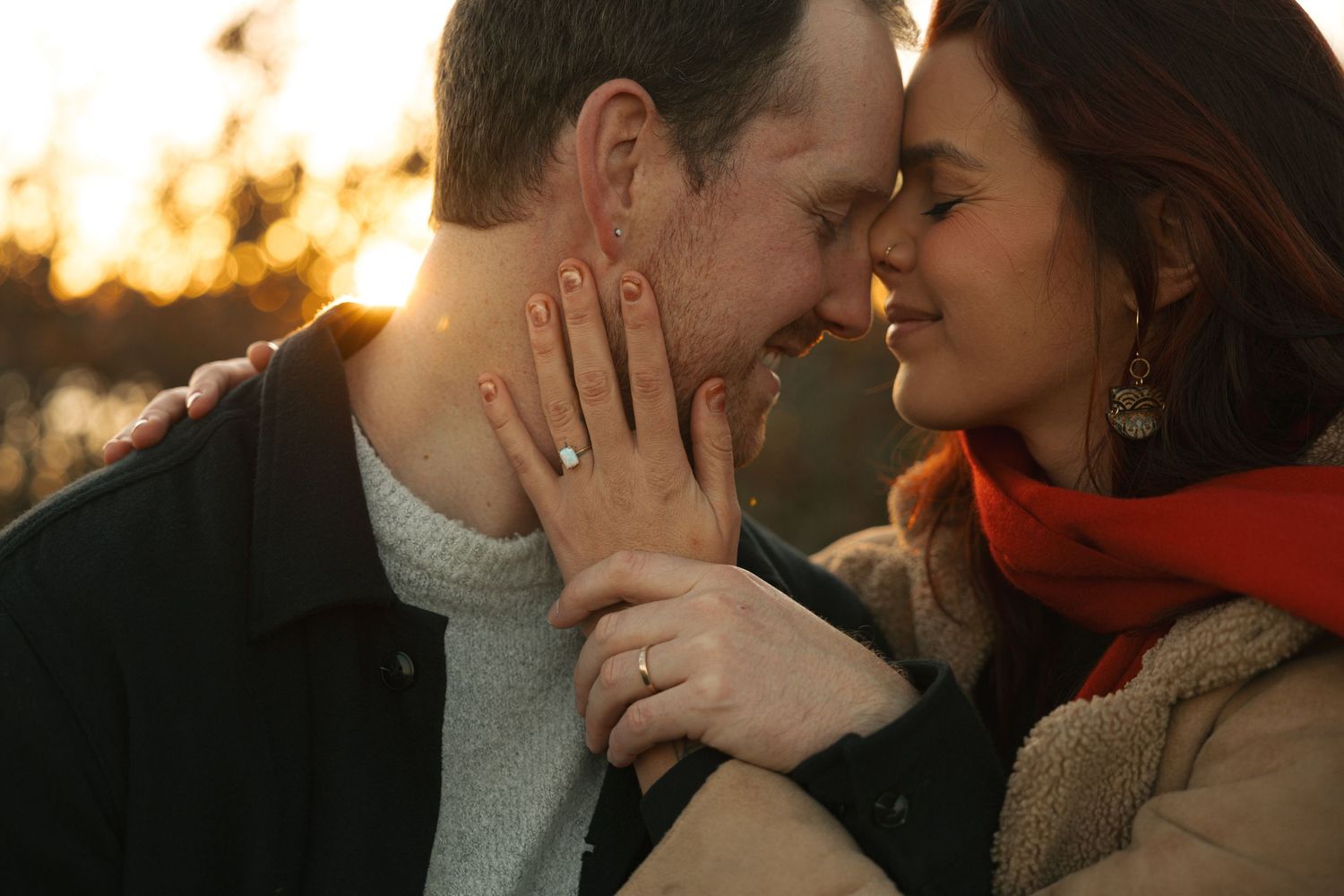 Romantic couple sharing an intimate moment at sunset, woman displaying engagement ring while touching man's face.