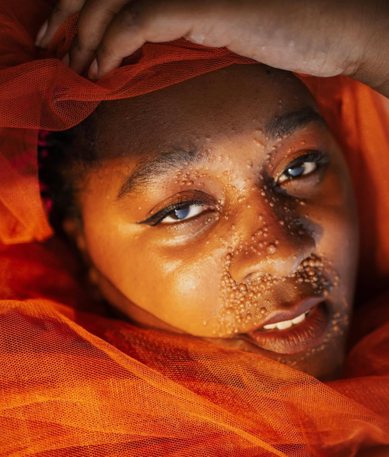 Close up portrait wrapped in orange fabric with glitter freckles and artistic makeup.