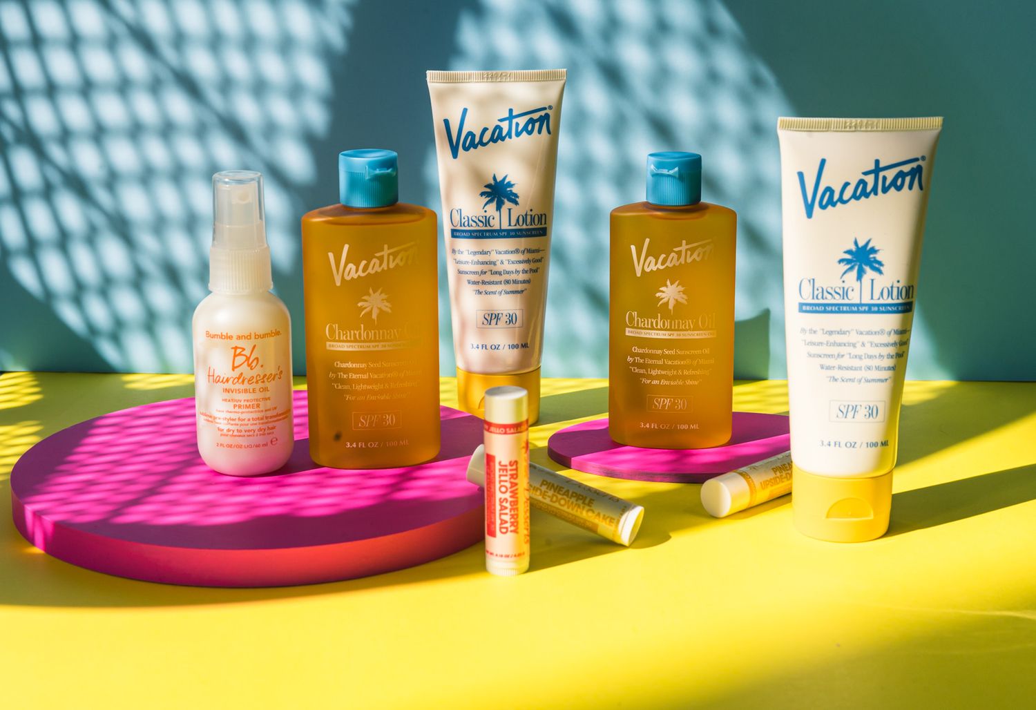Vacation skincare and sunscreen products displayed on pink and yellow surfaces with dramatic lighting.