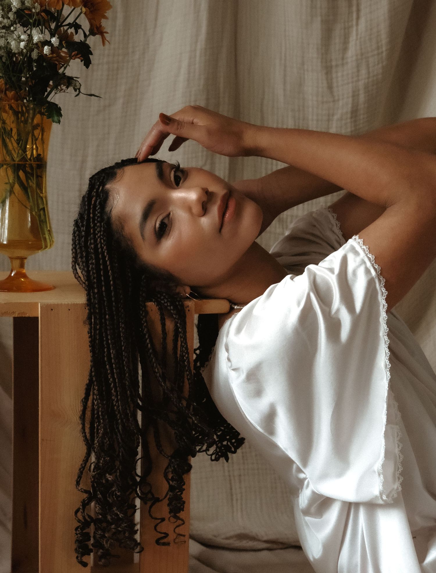 Artistic boudoir portrait with braided hair and silk dress near window light.