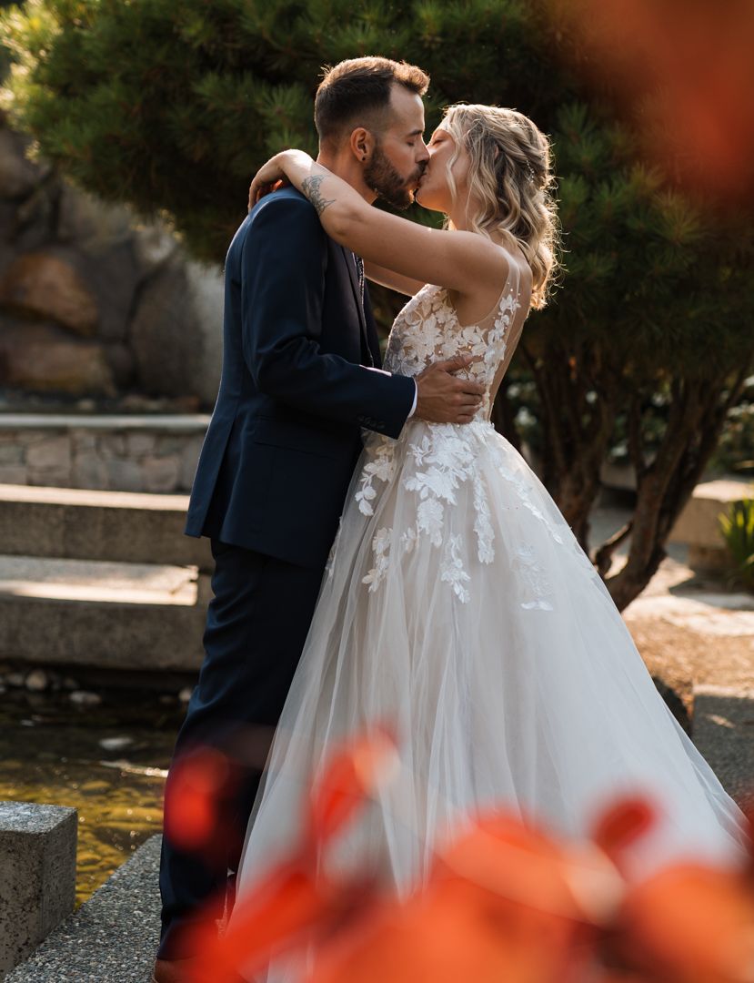 A romantic wedding couple sharing a kiss in their formal attire with beautiful autumn-tinted scenery in the background.