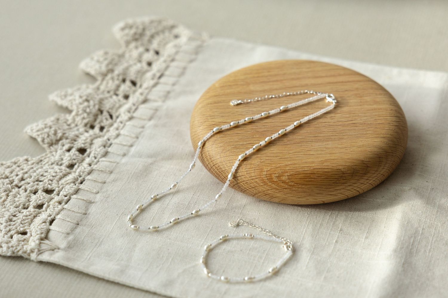 A wooden pendant necklace is shown in various stages of assembly against a textured white background.