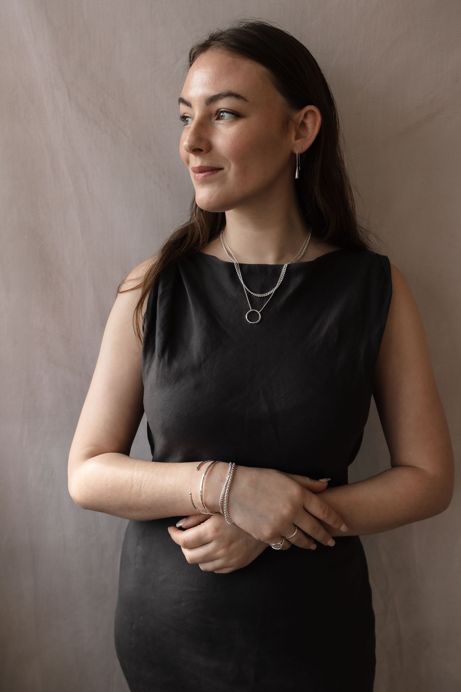 Woman wearing black sleeveless dress and layered necklaces against neutral backdrop.